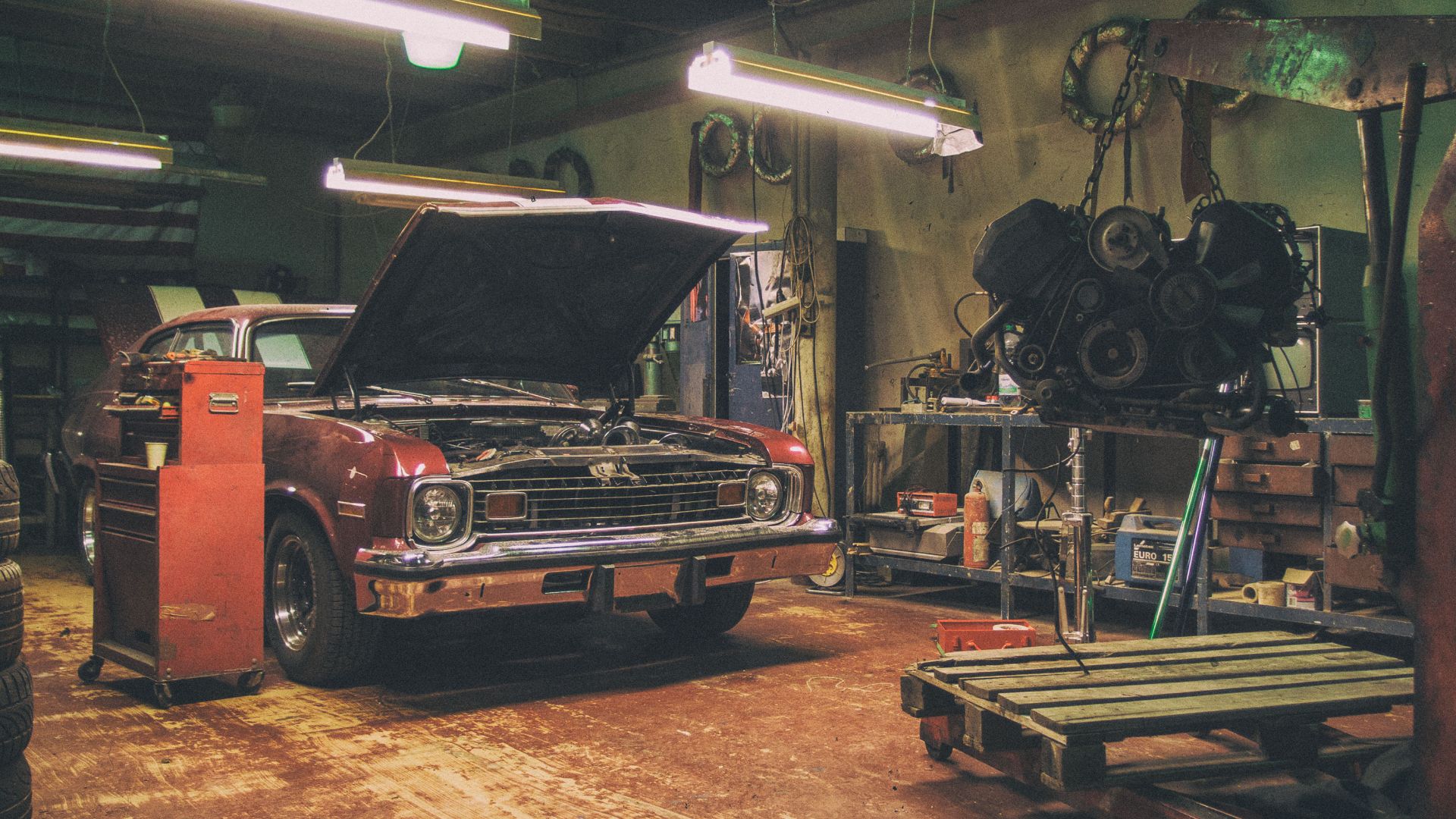 Vintage interior of a car repair shop with an old red American car and car engine on the crane. The automobile is ready for an engine replacement. Photographed by Martin Vorel - https://martinvorel.com