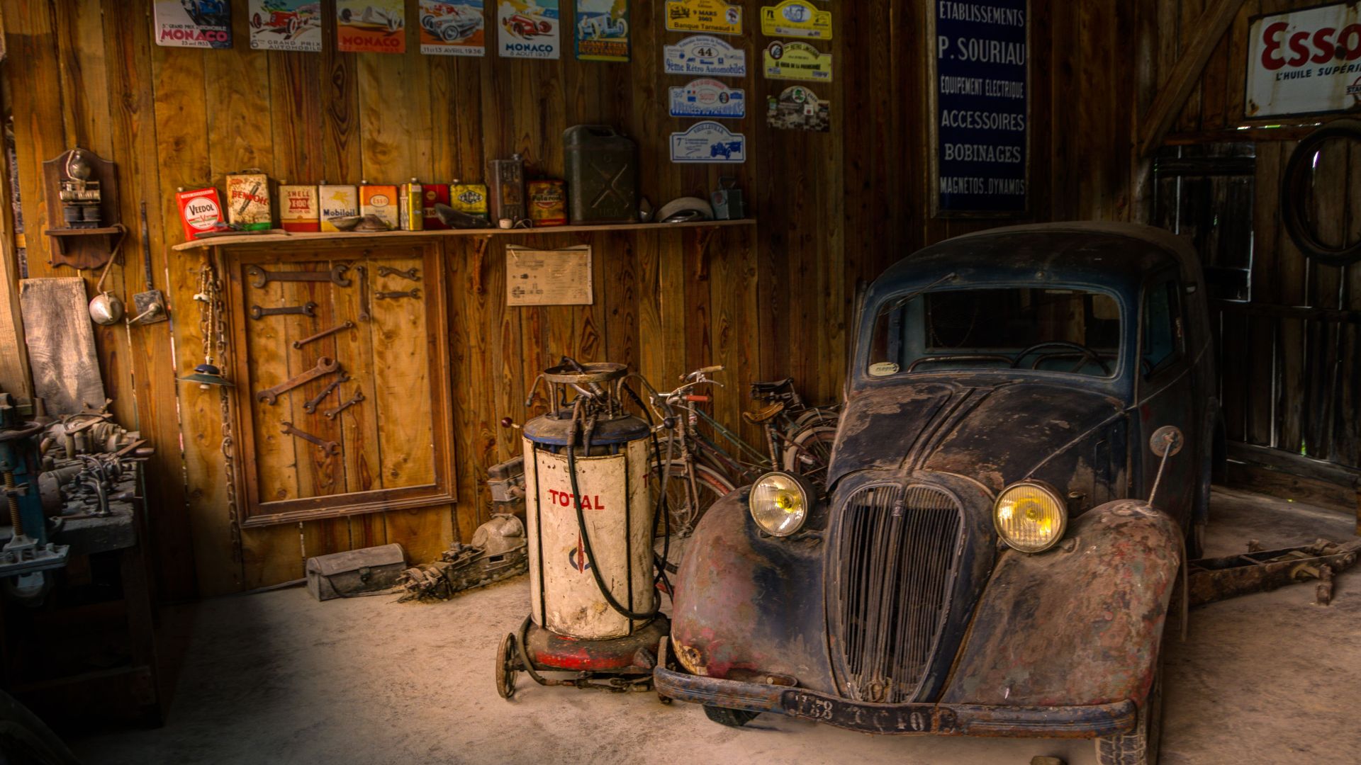 Old car in a rustic garage, surrounded by vintage signs and tools.