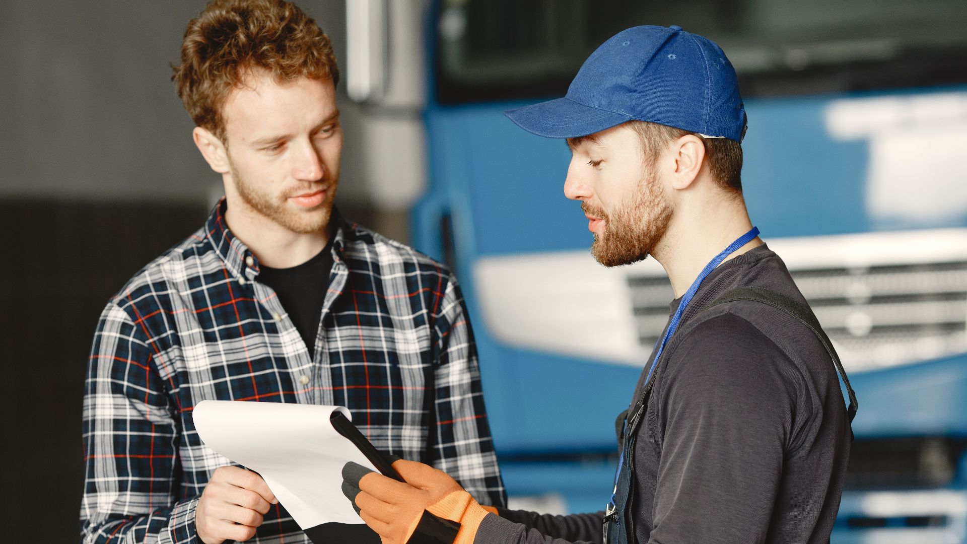 Mechanic in uniform talks with a customer about vehicle maintenance inside a garage.