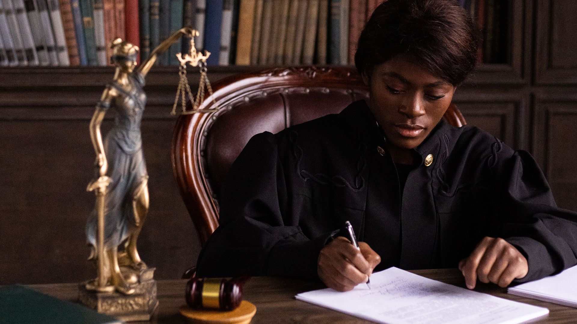 Black female judge sitting at desk in library, writing legal documents.