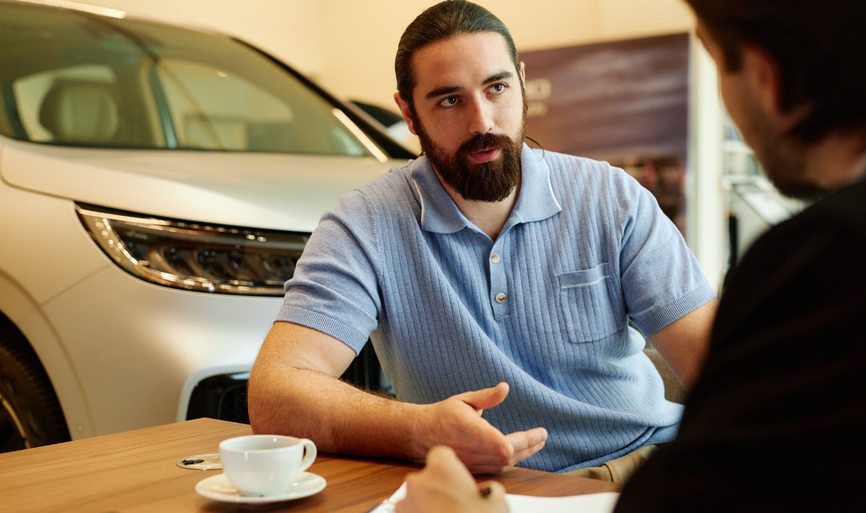 Medium shot of adult male client at desk discussing terms and conditions of purchase contract with auto dealer while buying new car at dealership center, copy space