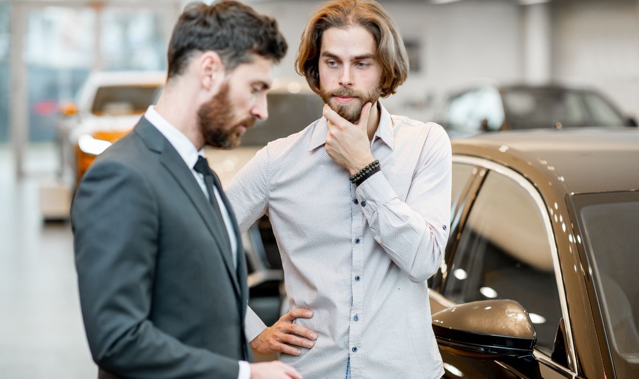 Man client hesitates choosing a car with salesperson in the showroom