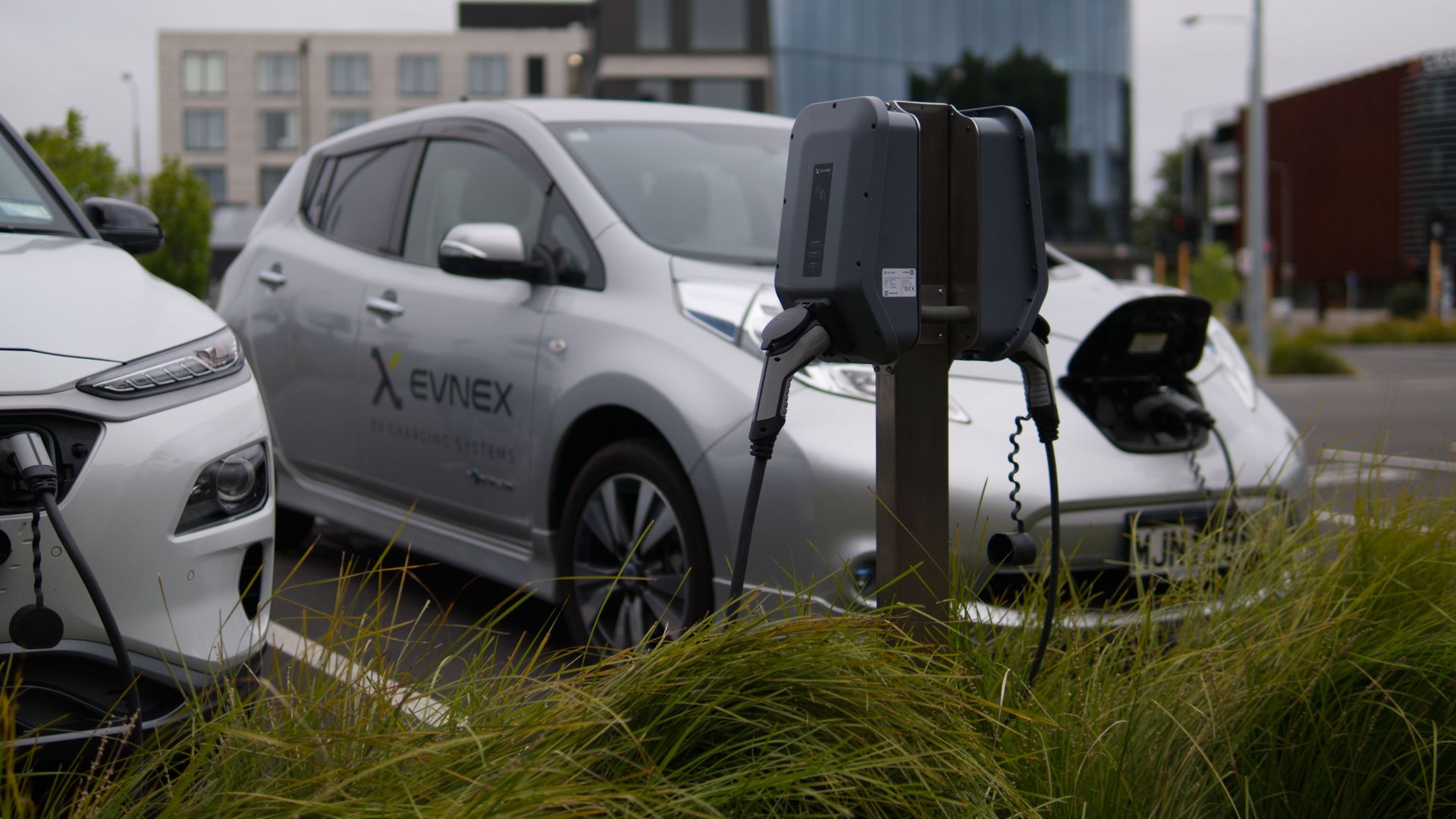 Electric vehicles at a charging station in Christchurch parking lot with modern architecture.