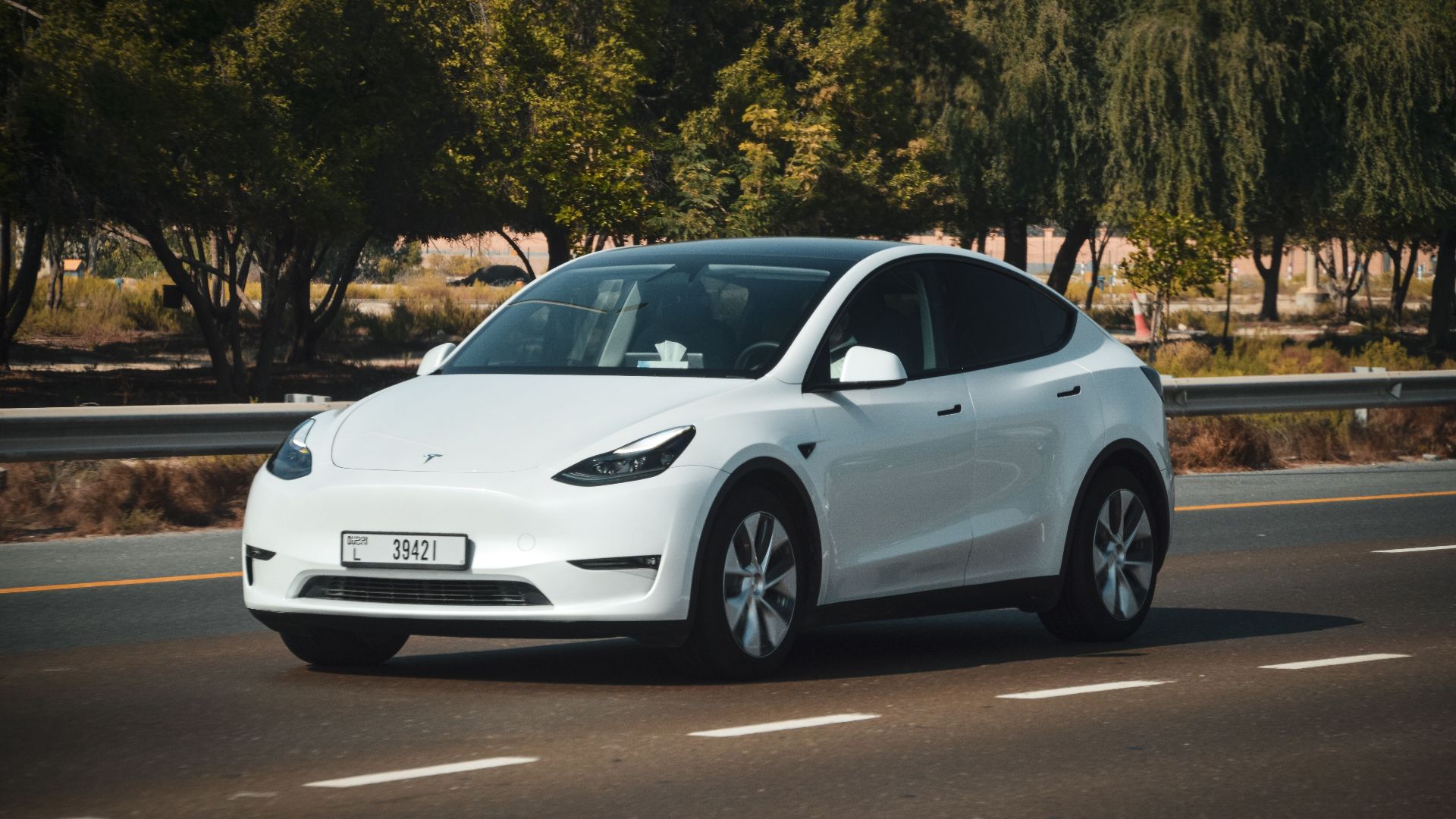 A sleek white electric car cruising on a sunny highway in Abu Dhabi, UAE.