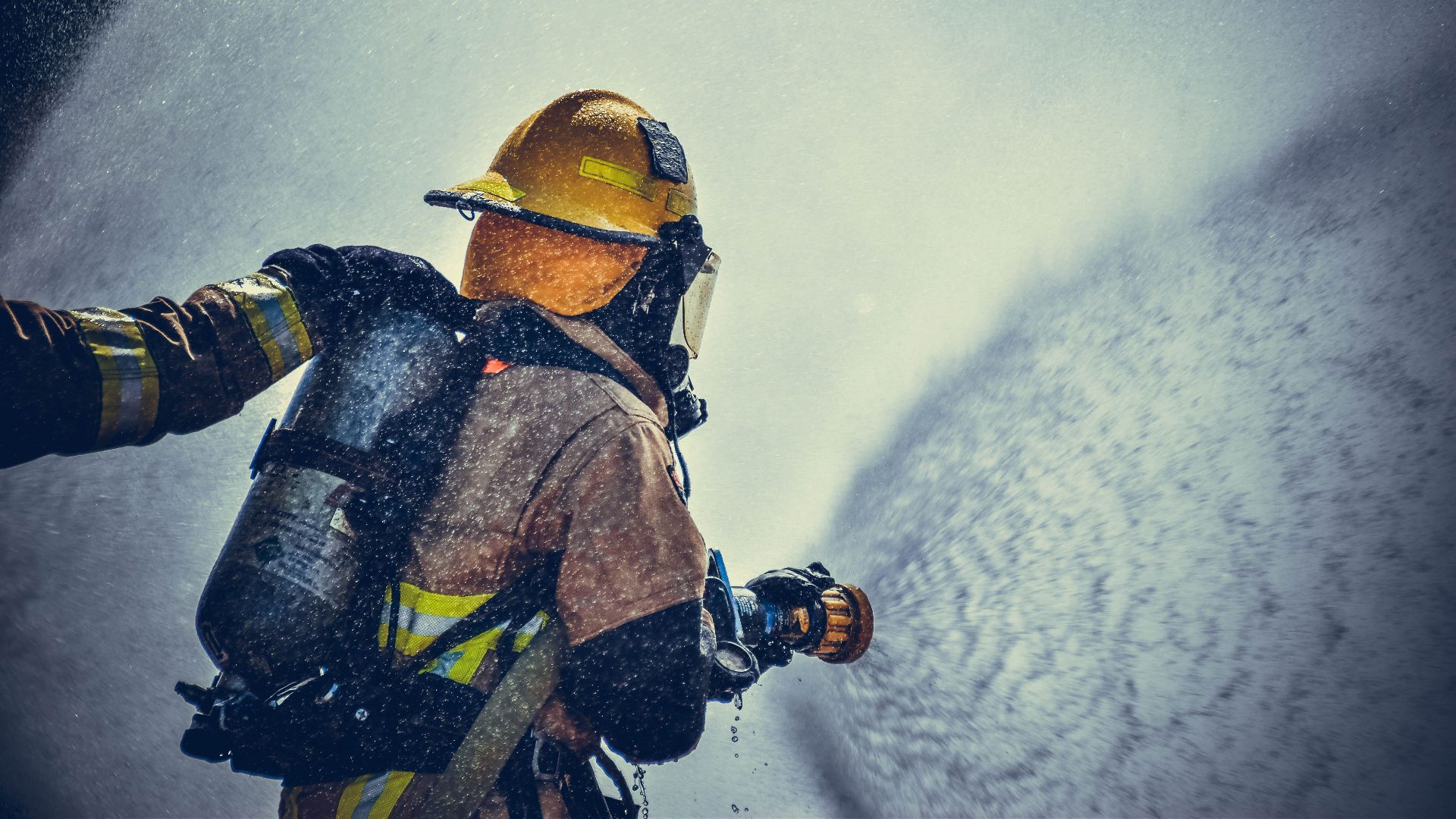 A brave firefighter in protective gear sprays water during training or emergency.