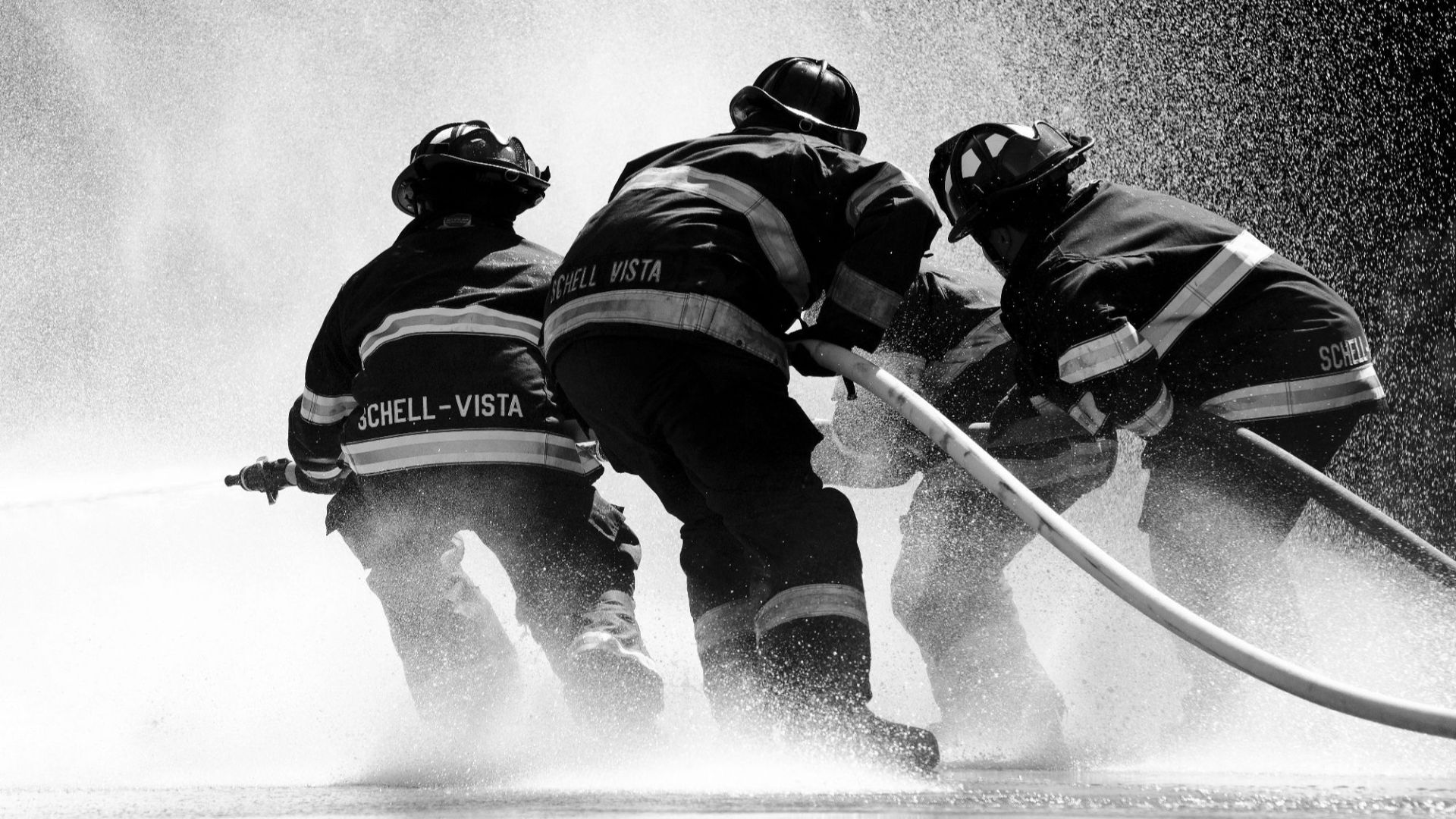 Firefighters in full gear battle heavy water spray in an intense operation.