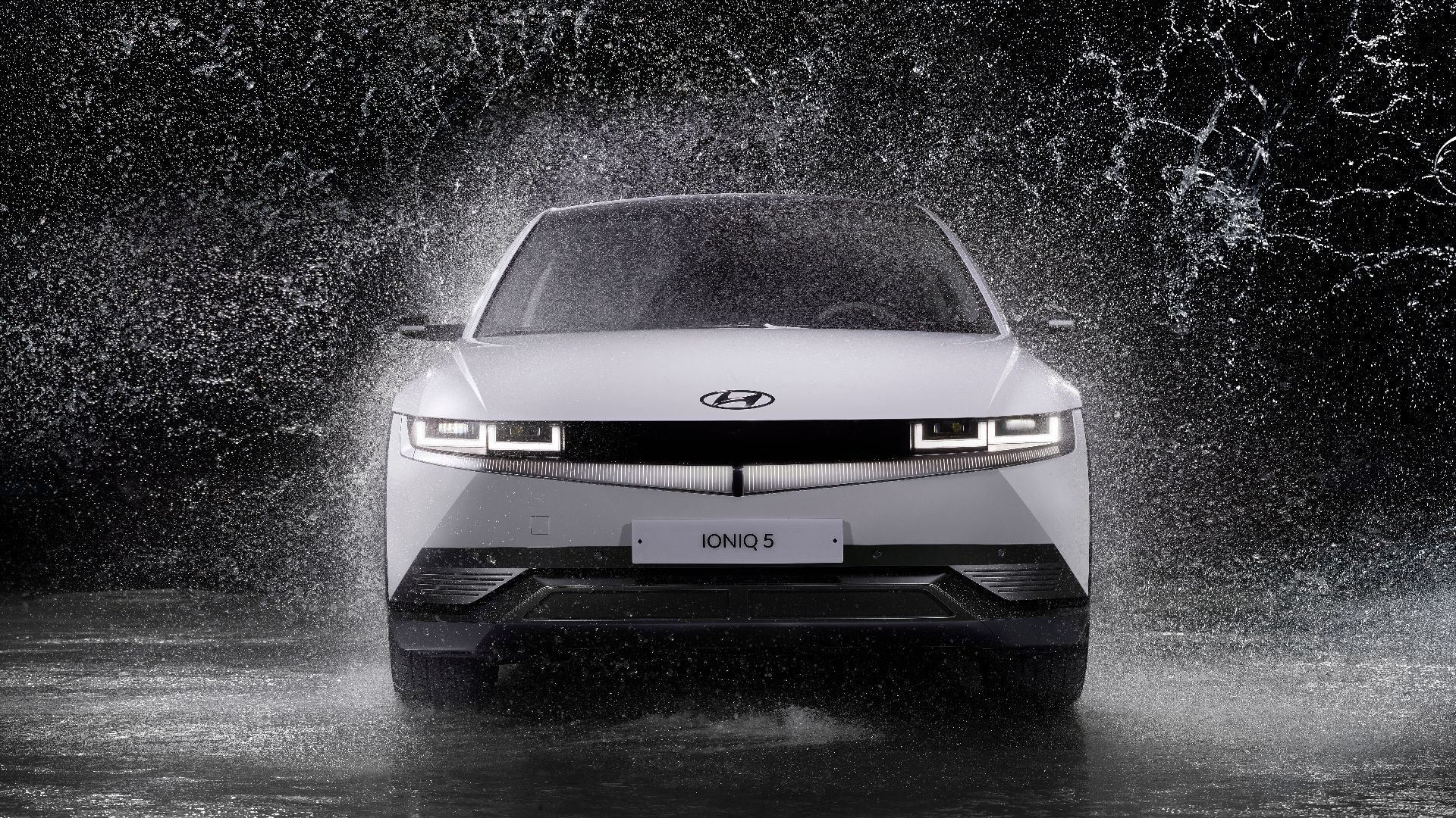 Dynamic front view of a Hyundai Ioniq 5 splashing through rain, captured in black and white.
