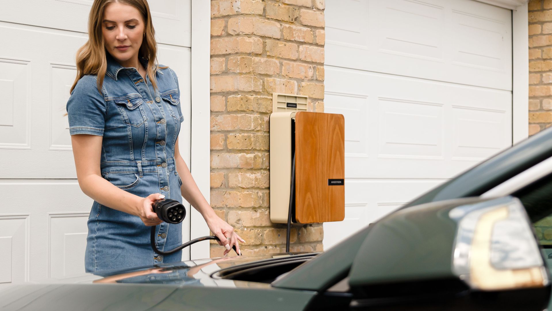 A woman plugs in an electric vehicle charger at a home charging station.