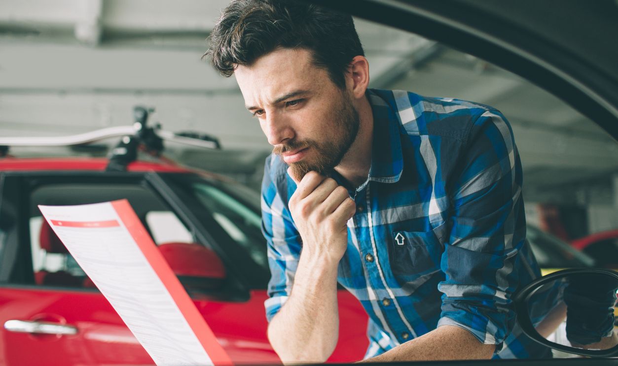 Perfect lines. The young dark-haired bearded man examining car at the dealership and making his choice. Horizontal portrait of a young guy at the car. He is thinking if he should buy it