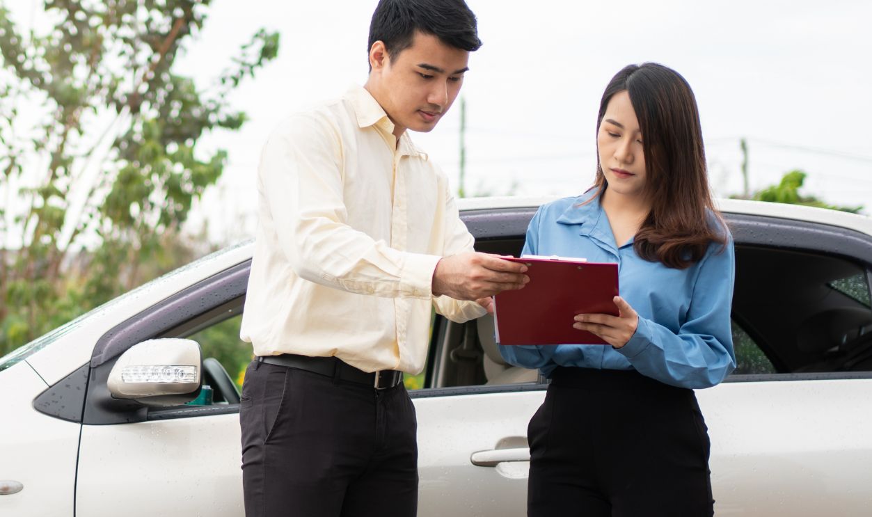 Asian women driver Talk to Insurance Agent for examining damaged car and customer checking on report claim form after an accident. Concept of insurance and car traffic accidents.