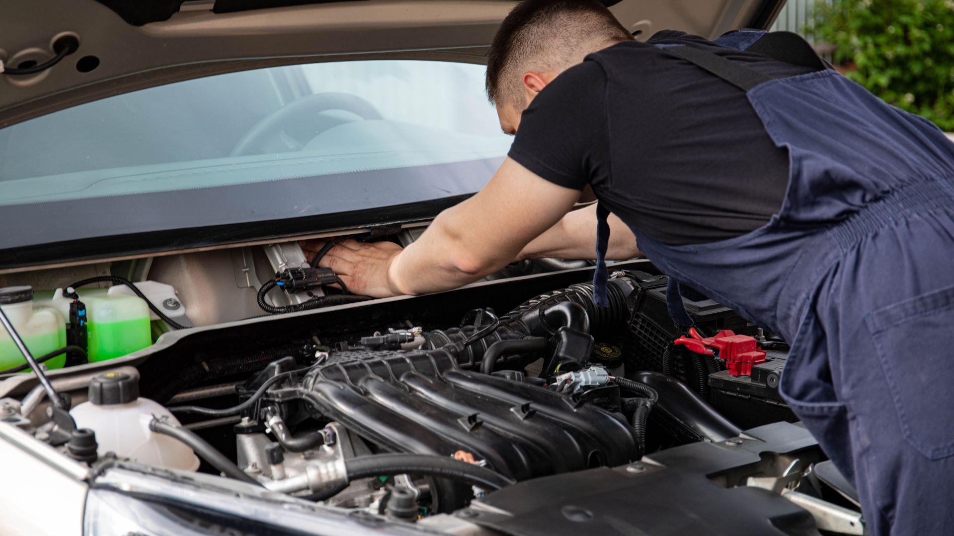 Auto mechanic performs engine maintenance on a car. Focus on hands and engine components.