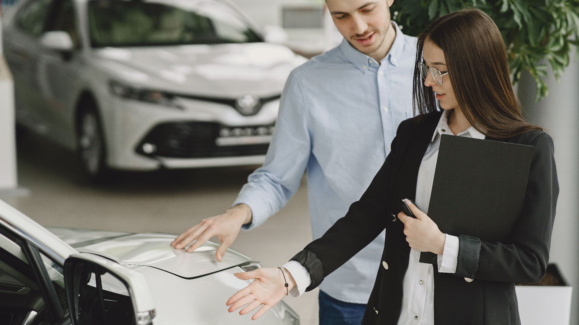 A man and saleswoman discussing a hybrid vehicle's features in an indoor showroom.