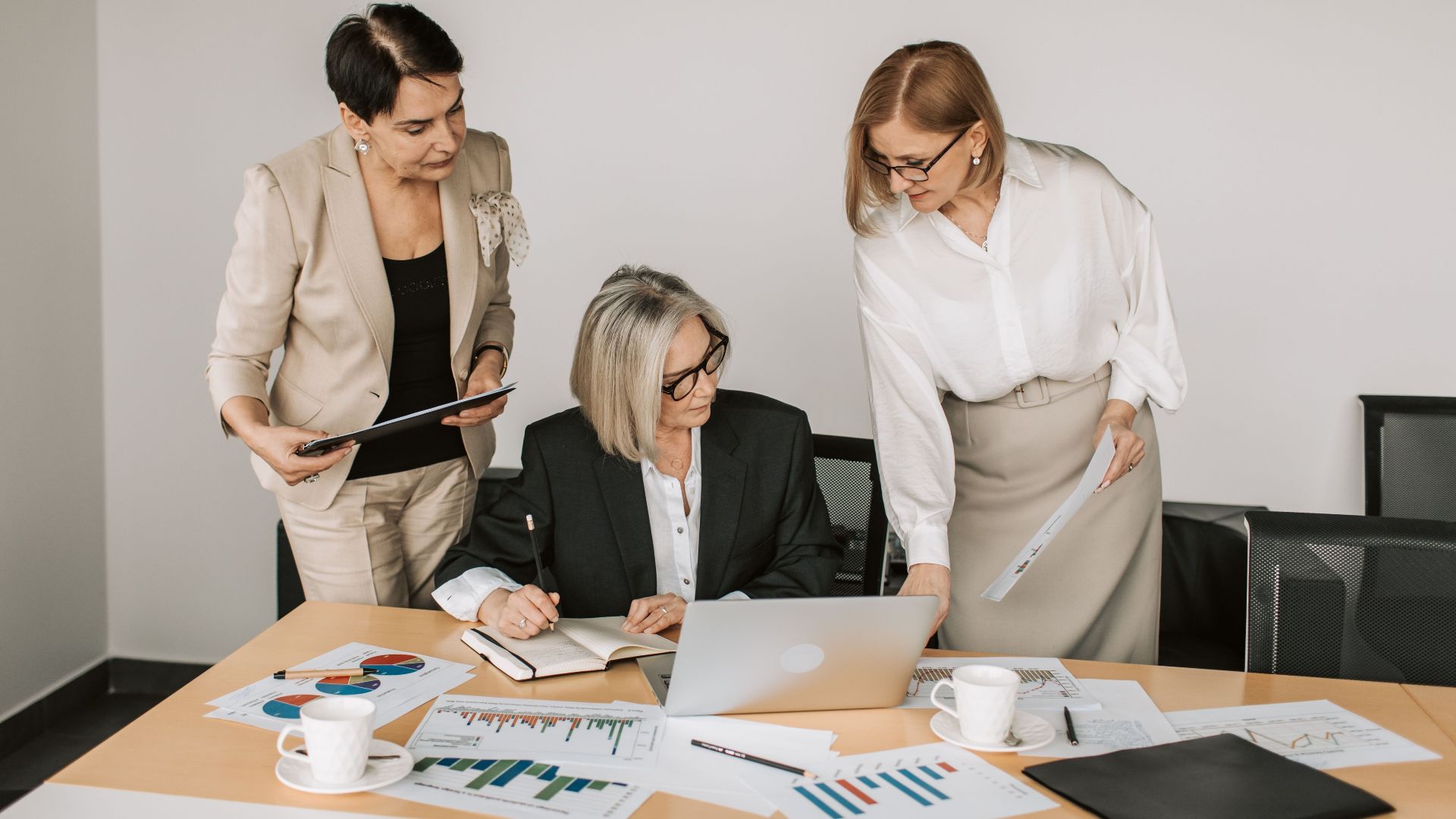 Three businesswomen discussing documents during a meeting in a modern office setting.