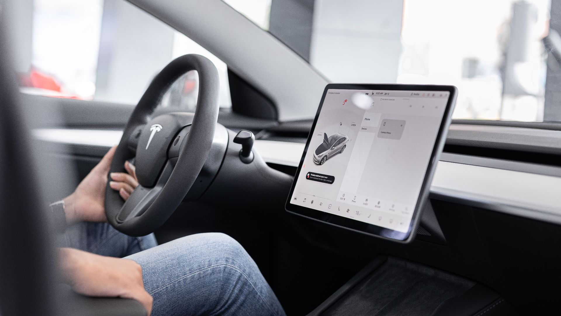 Interior of an electric car showing steering wheel and large touchscreen display, indicating modern technology.