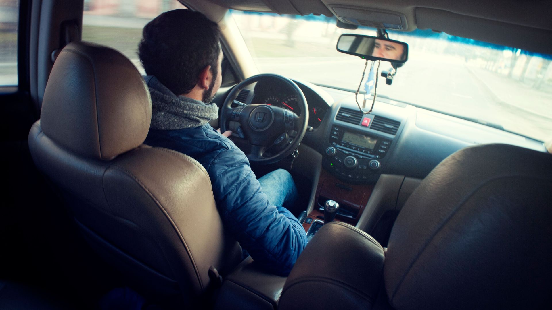 A man driving a car with focus on interior, dashboard, and steering wheel, captured from the backseat.