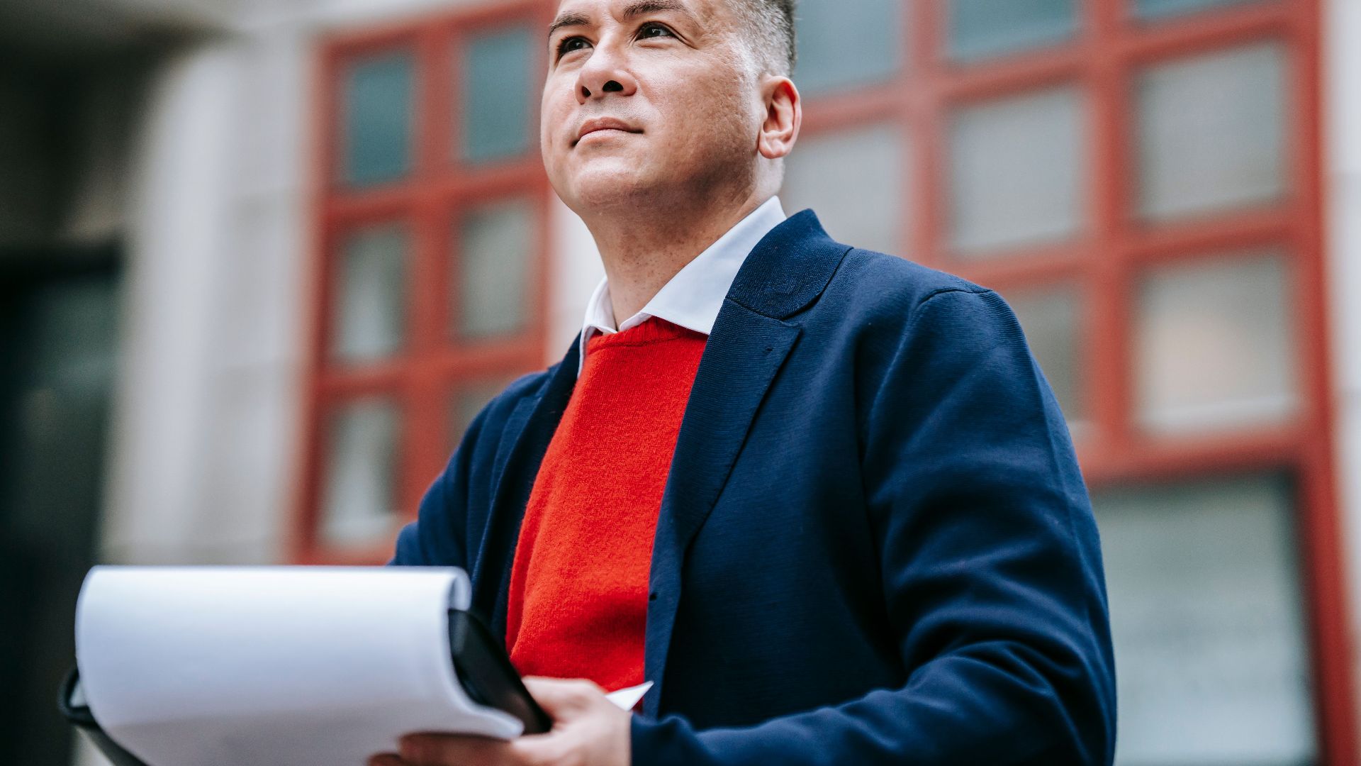 A confident businessman in a stylish outfit reviewing documents outdoors in a professional setting.