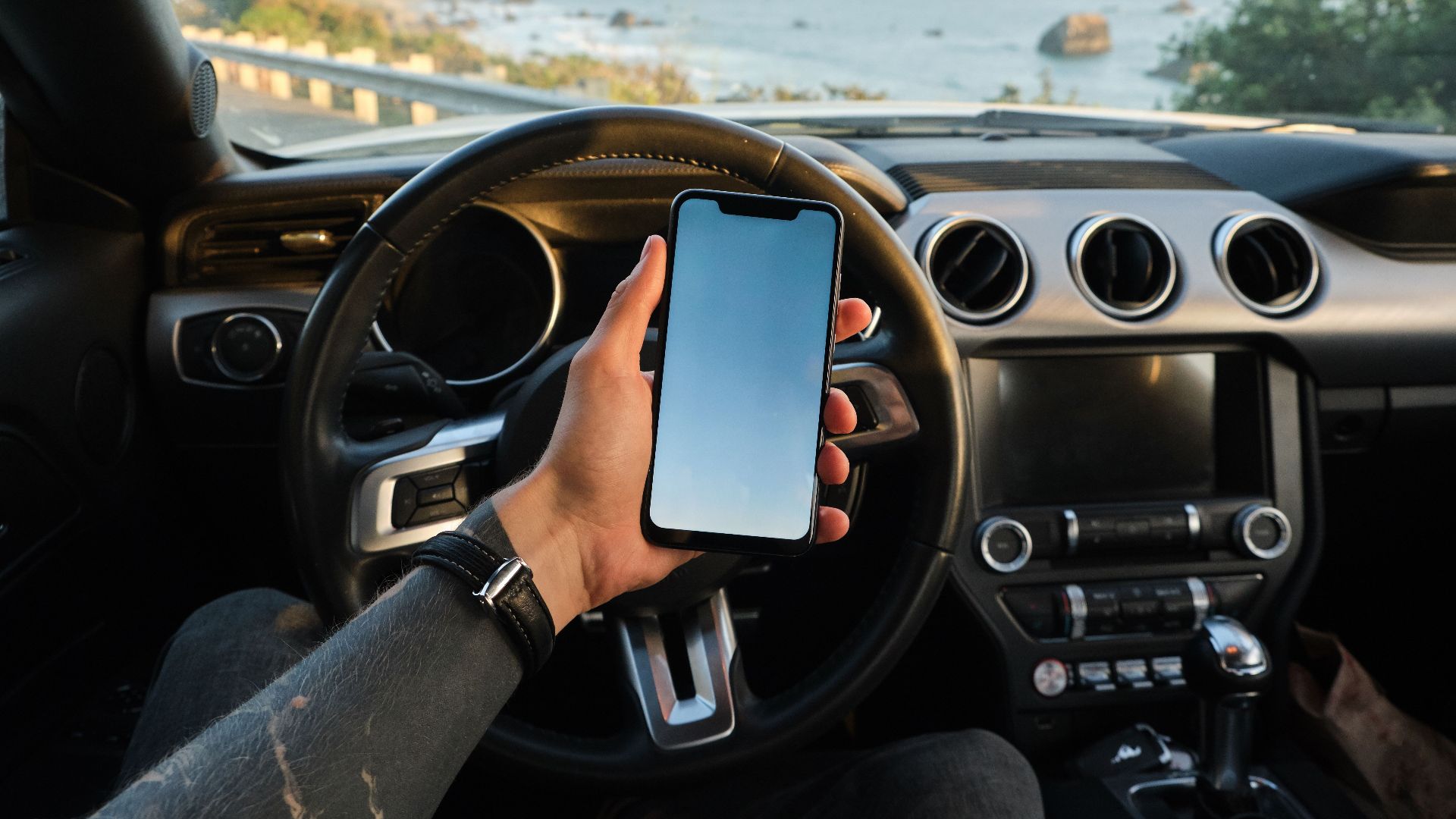 Crop anonymous guy with tattoo on hand navigating on mobile phone while driving car near sea