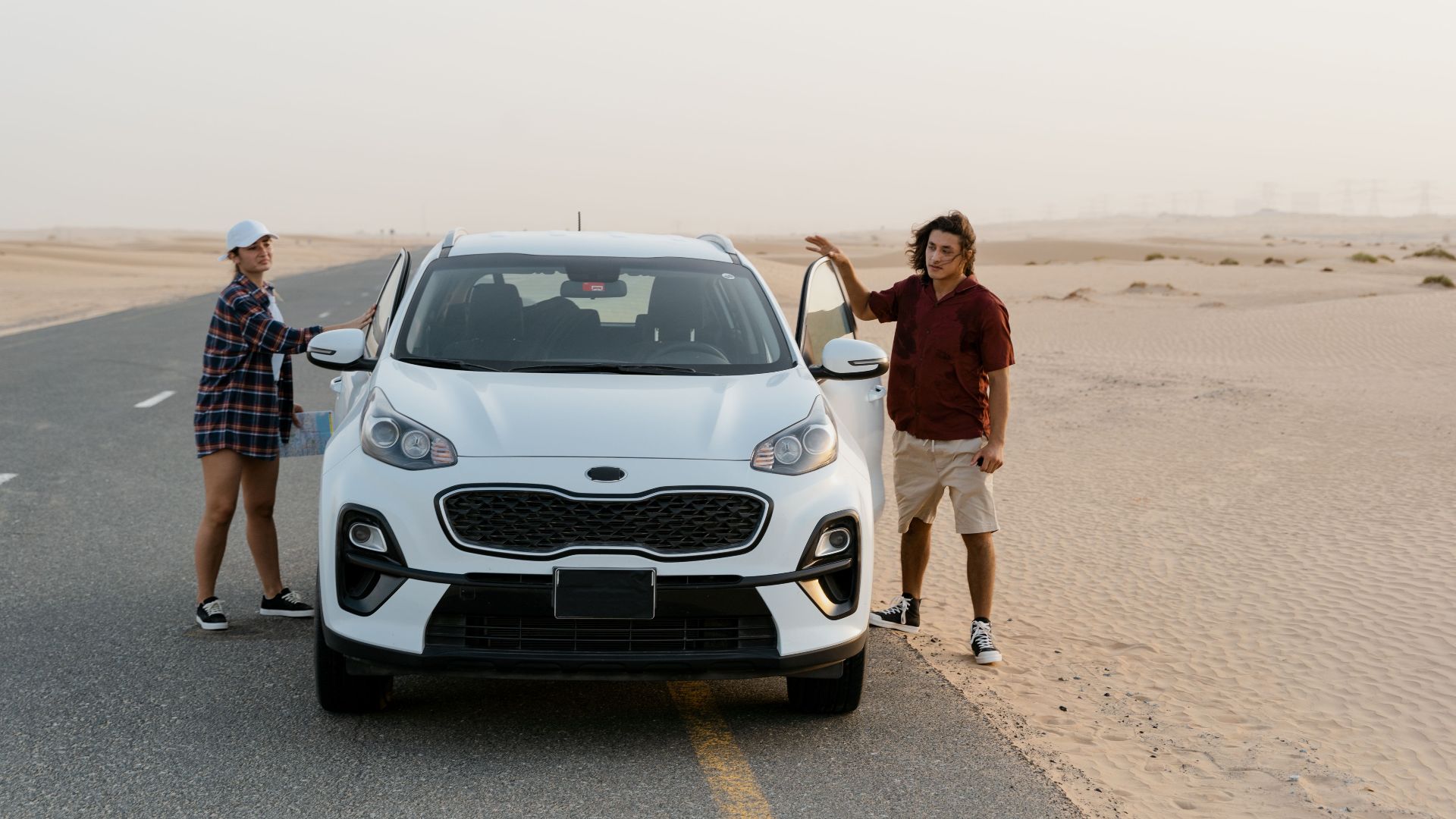 A couple stands by their SUV on a desert road, enjoying a scenic road trip.