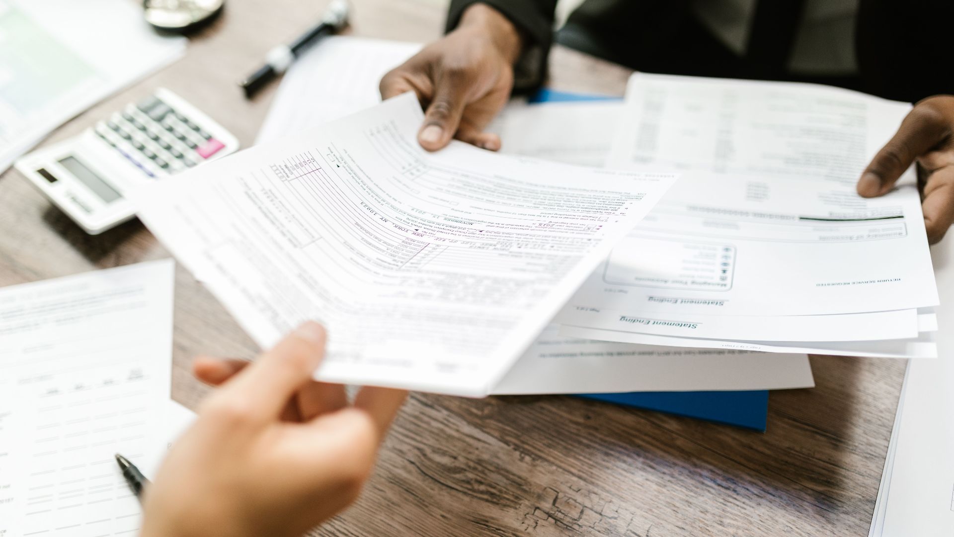 Two professionals exchanging documents in an office setting, focusing on paperwork and data analysis.