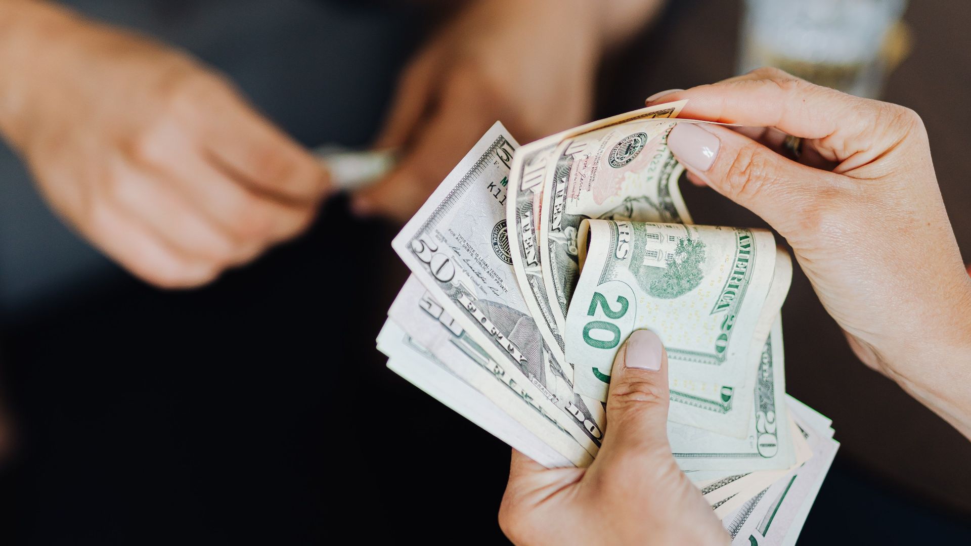 Hands exchanging cash in an indoor setting, representing financial transaction or budgeting.