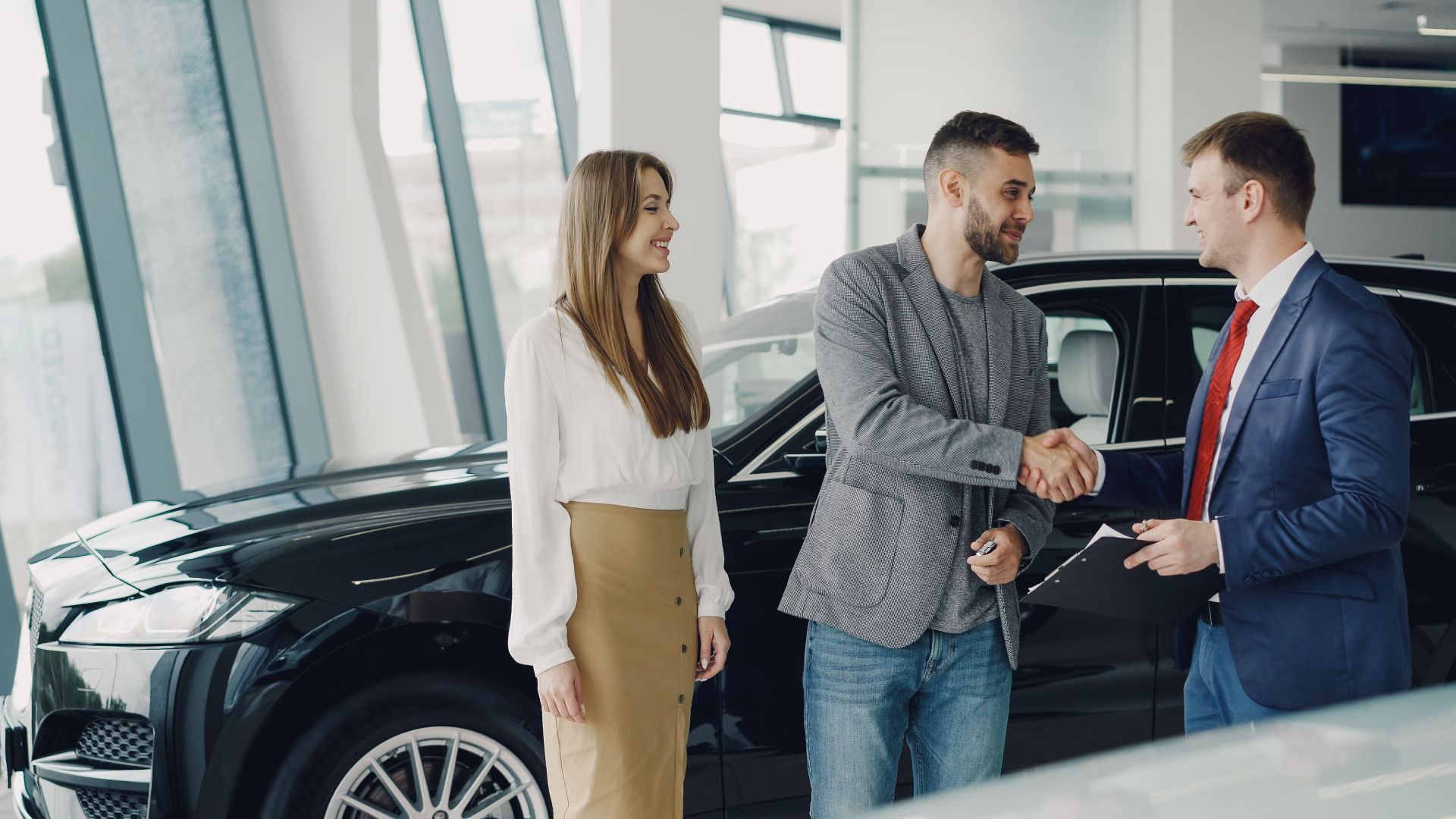 Customers shaking hands with dealer in showroom, sealing car purchase deal.