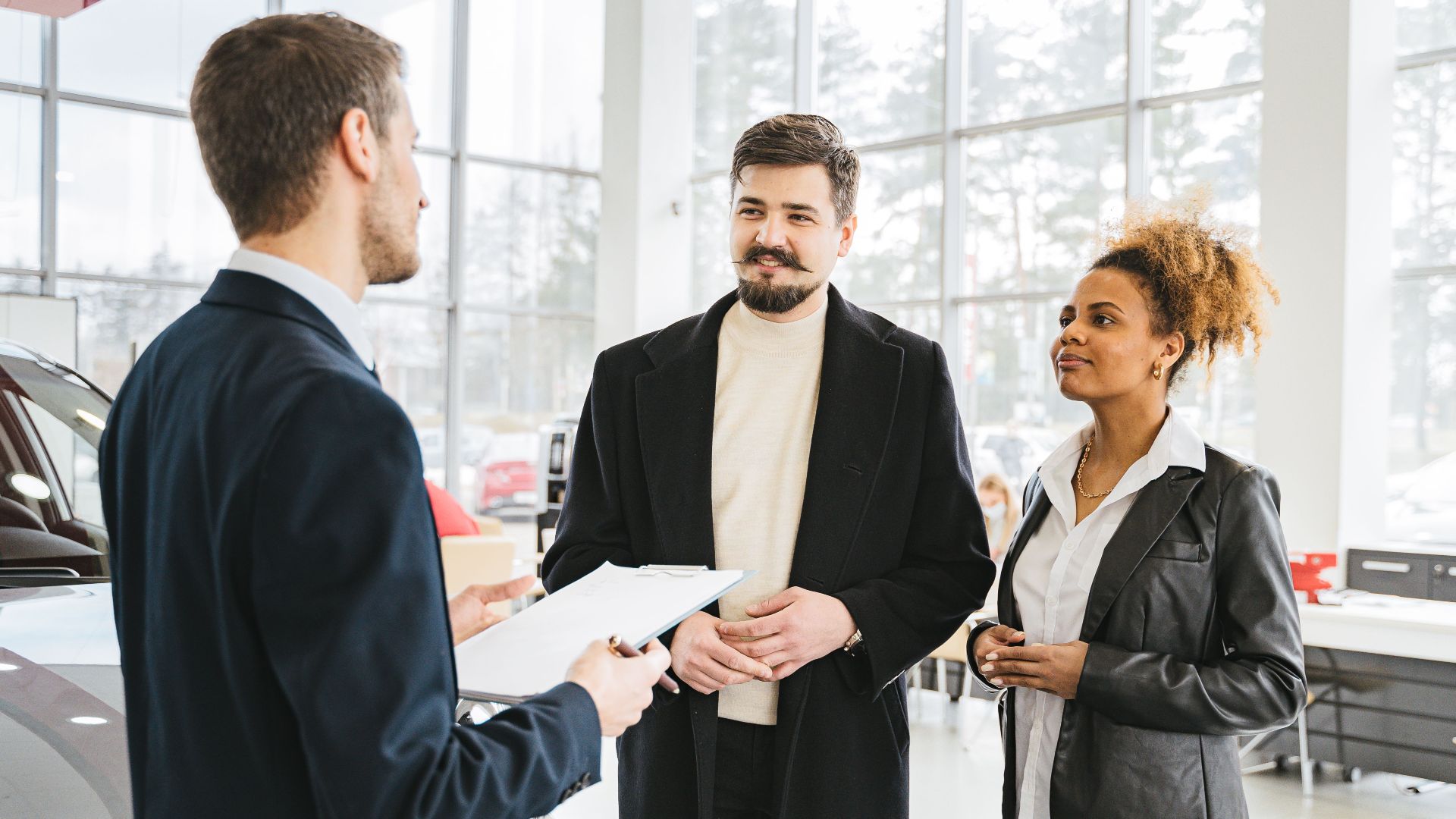 Happy couple discussing car purchase with dealer in showroom. Professional interaction and consultation.