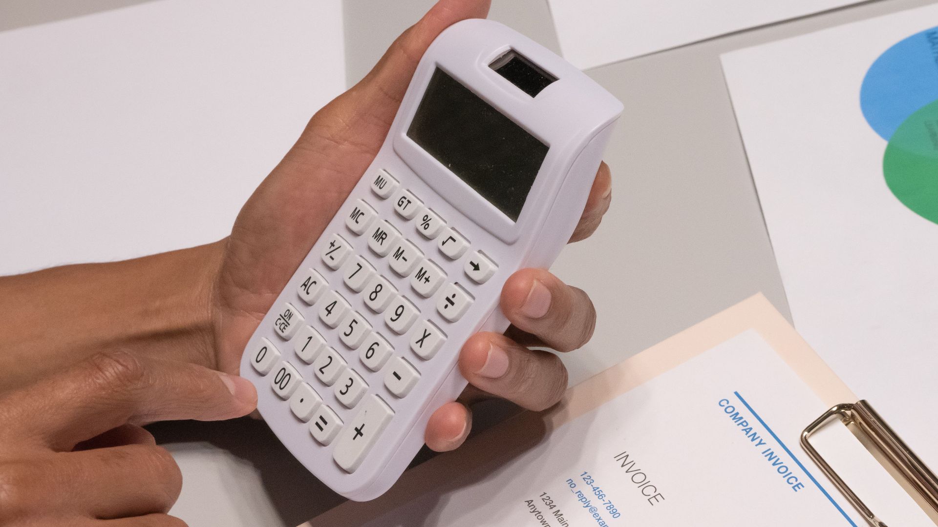 Close-up of hands using a calculator next to a company invoice, depicting a financial calculation concept.