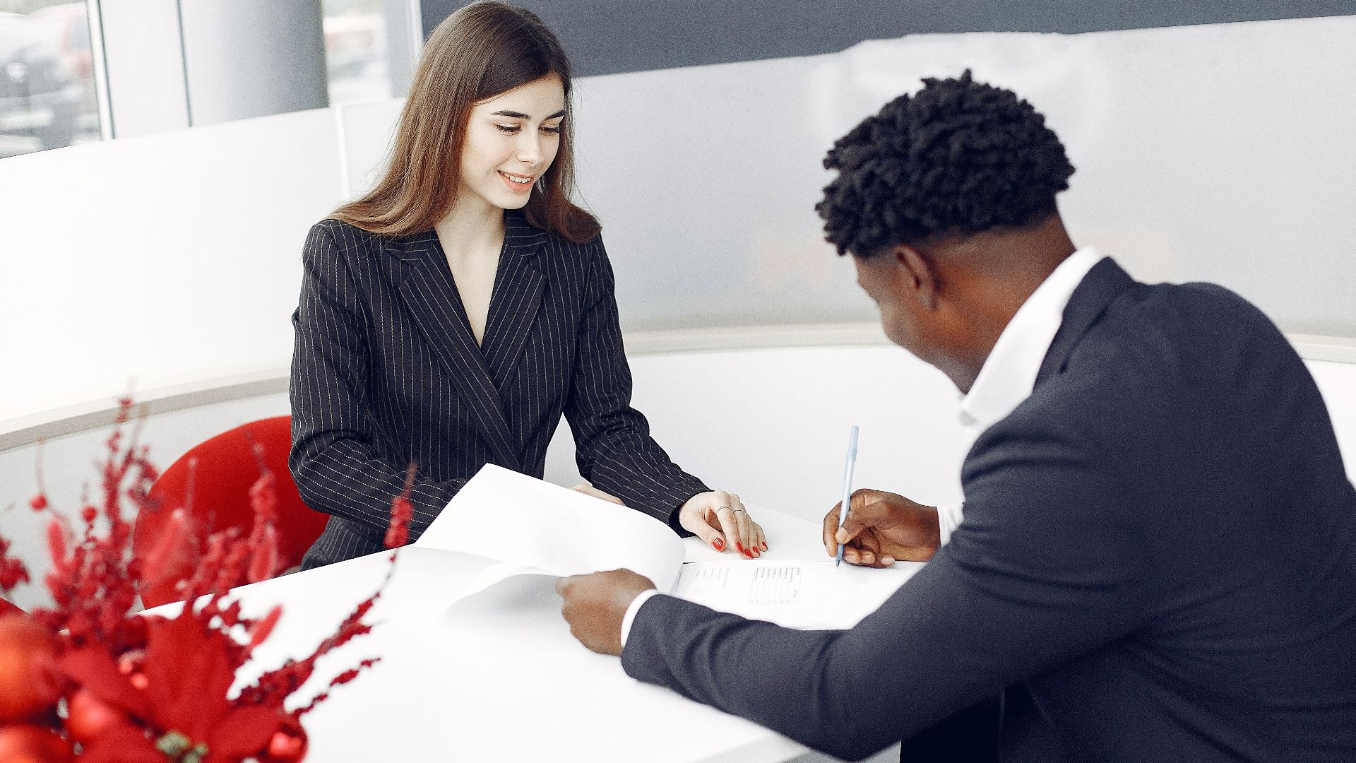Positive stylish multiethnic buyer in formal classy suit and agent signing papers in modern light creative office in daylight and smiling happily
