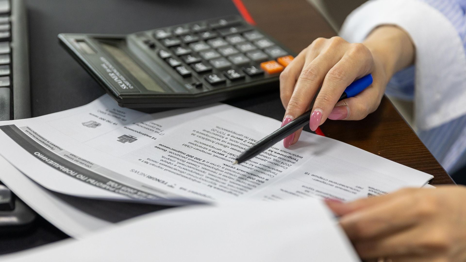 Close-up of a woman's hand reviewing financial documents with a calculator.