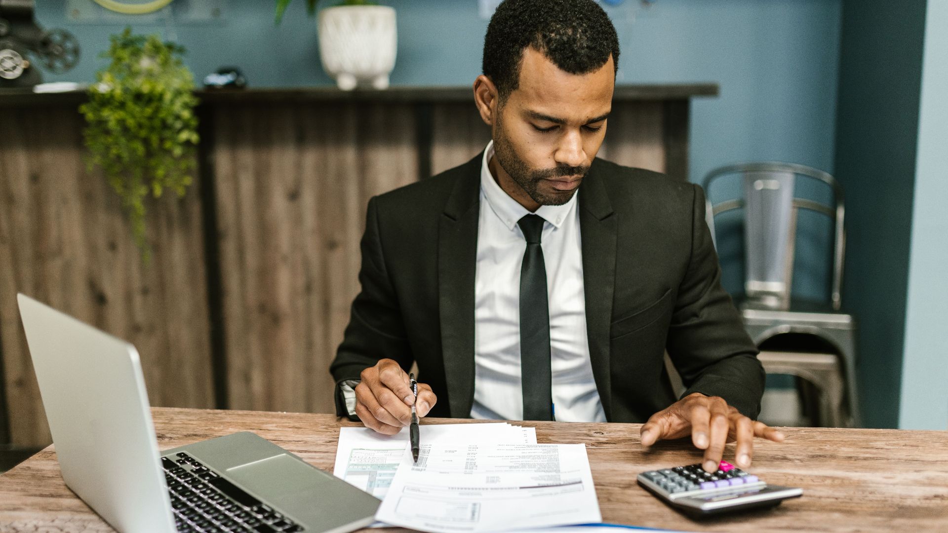 A focused businessman works with a calculator and documents in a modern office.