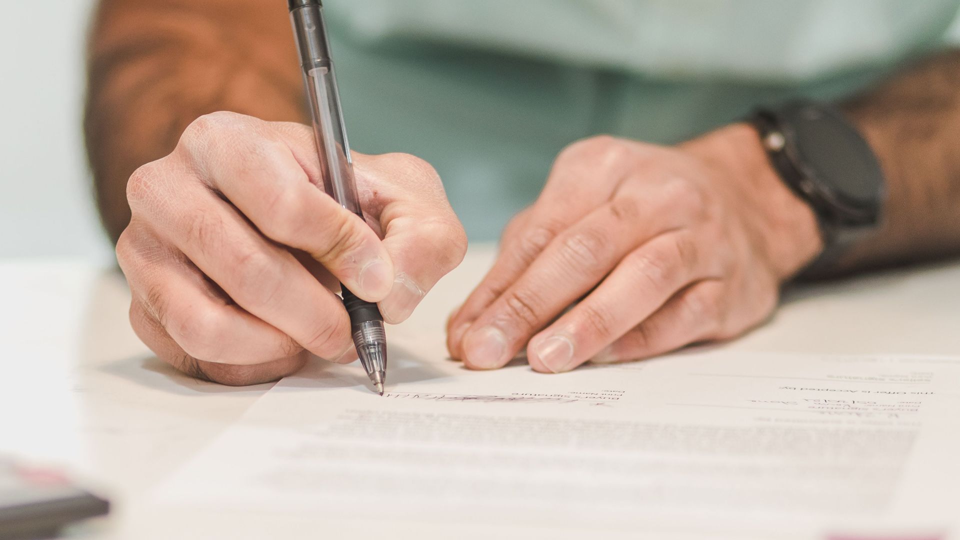 Close-up of a man signing an official document with a ballpoint pen on a desk.