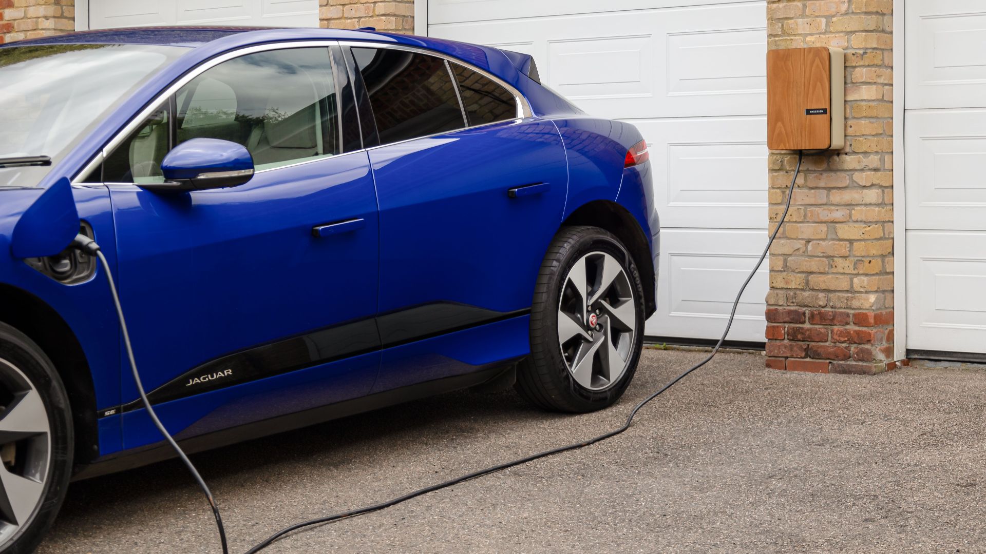 Blue electric vehicle charging at home using wall-mounted unit. Sustainable transportation solution.