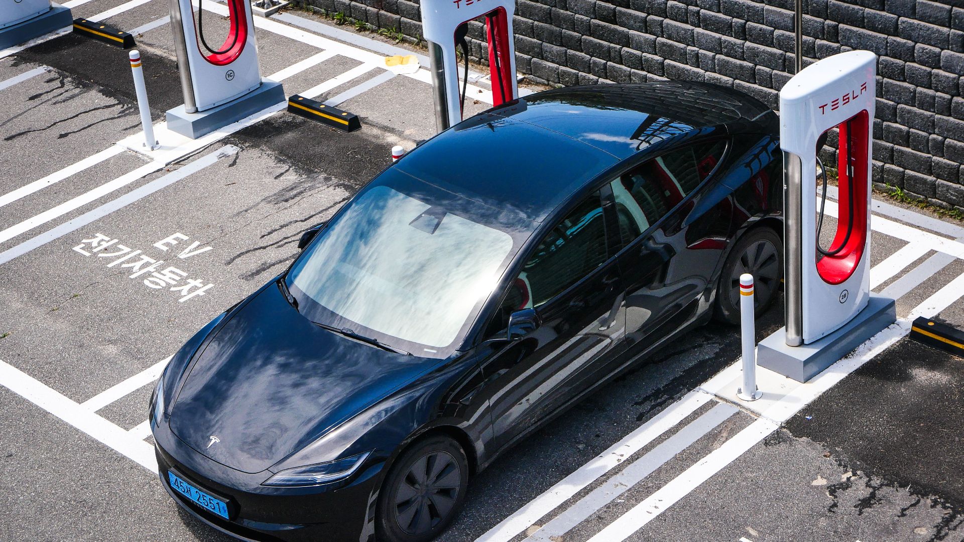 A black Tesla parked at a charging station in an urban setting.