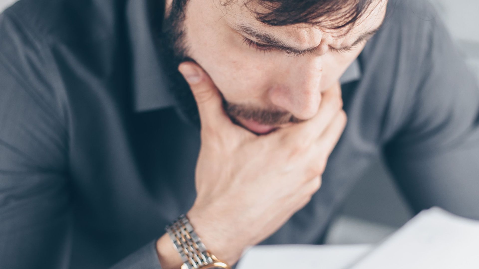 Man in gray shirt with glasses looking concerned over financial papers.