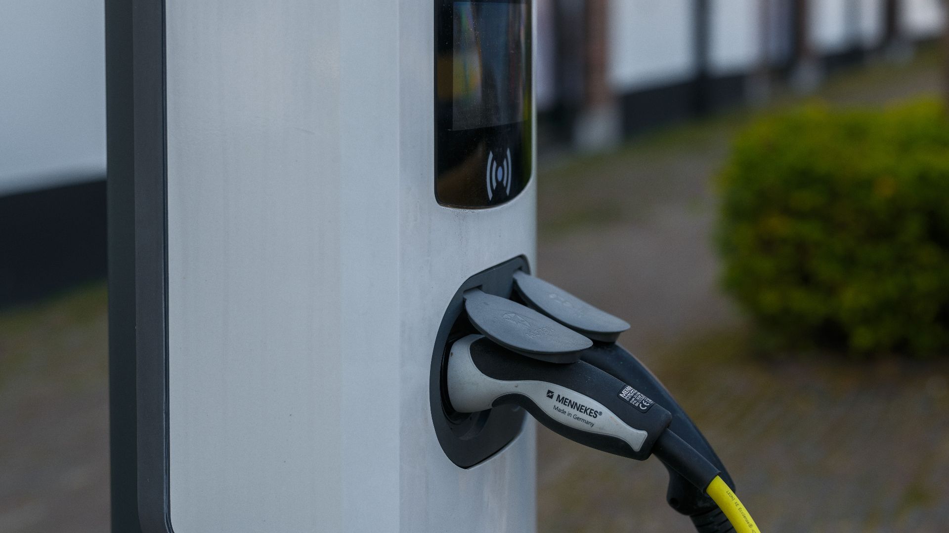 Close-up of an electric vehicle charging station with cable and plug outdoors.