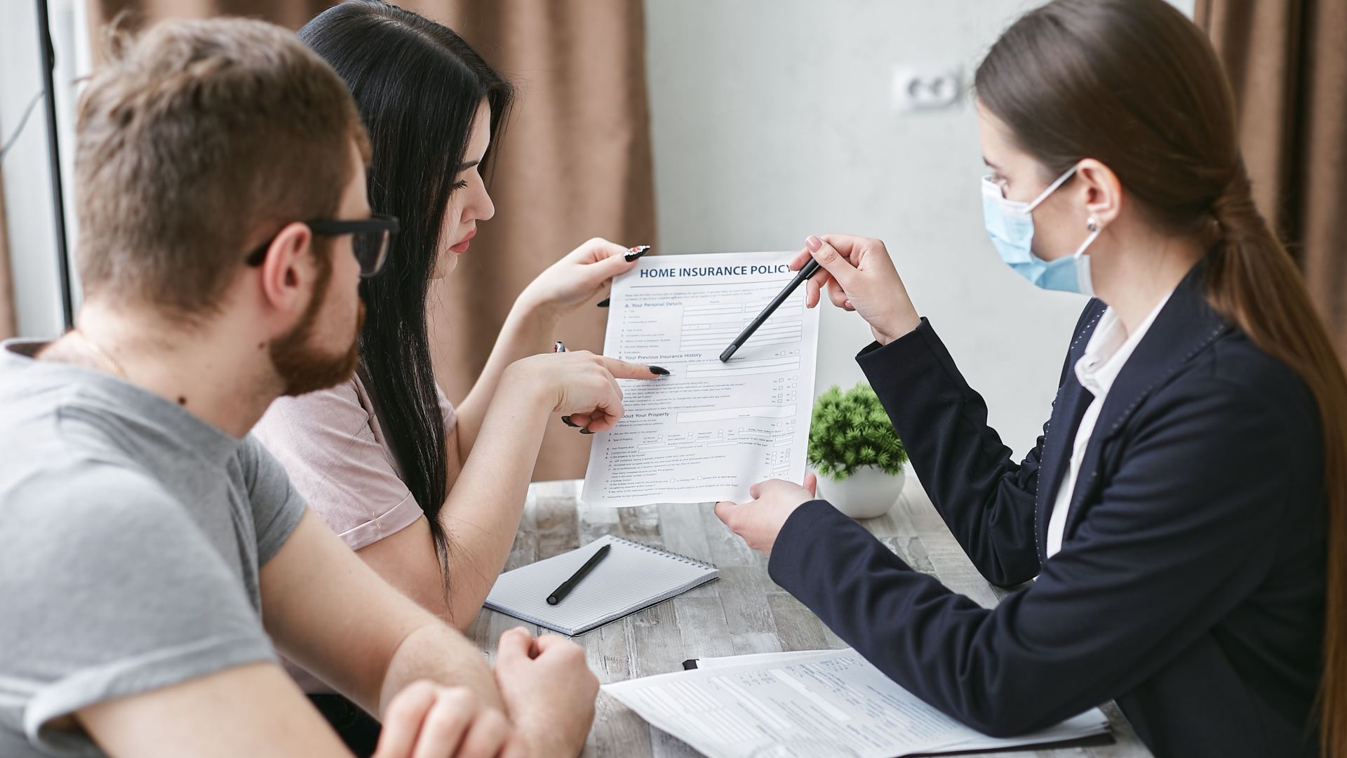 Three adults discuss a home insurance policy at a meeting table indoors.