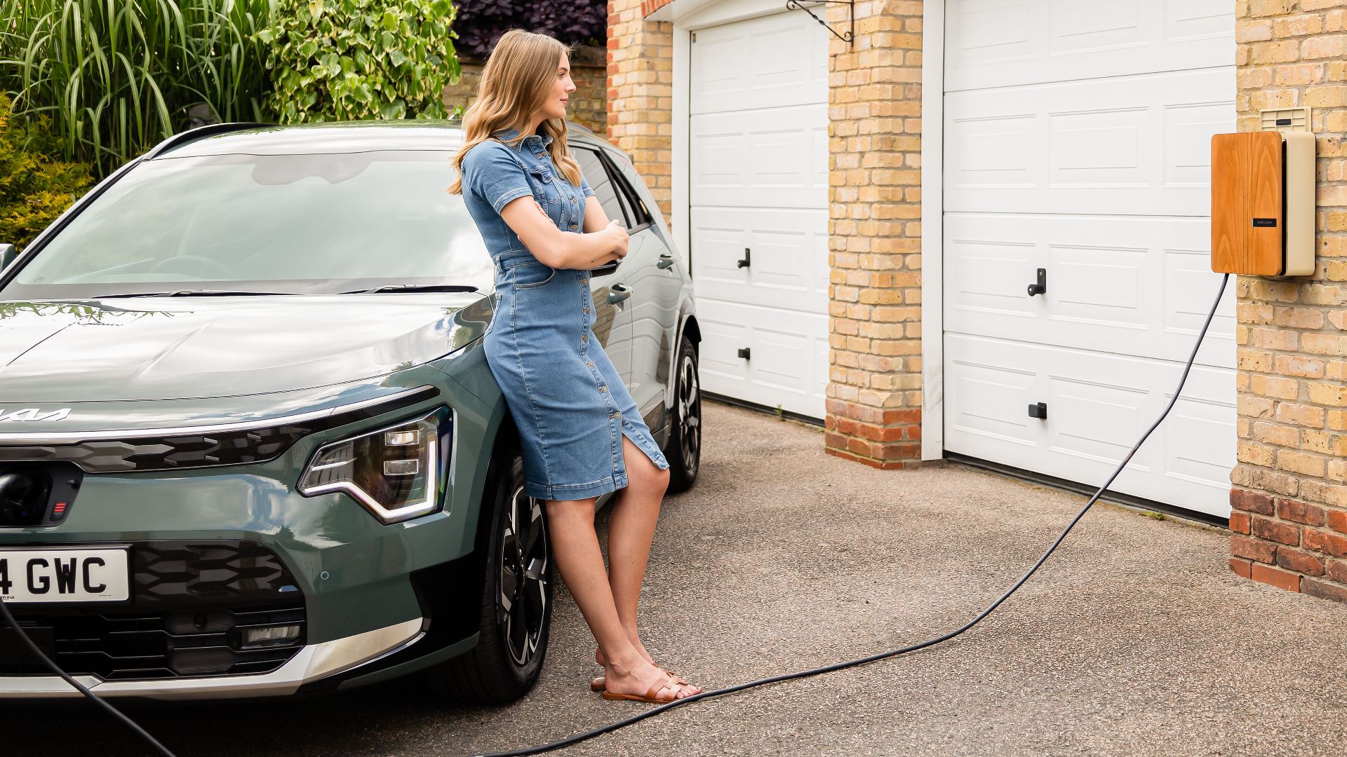 Woman charging electric vehicle at home with a modern wall-mounted charging station.