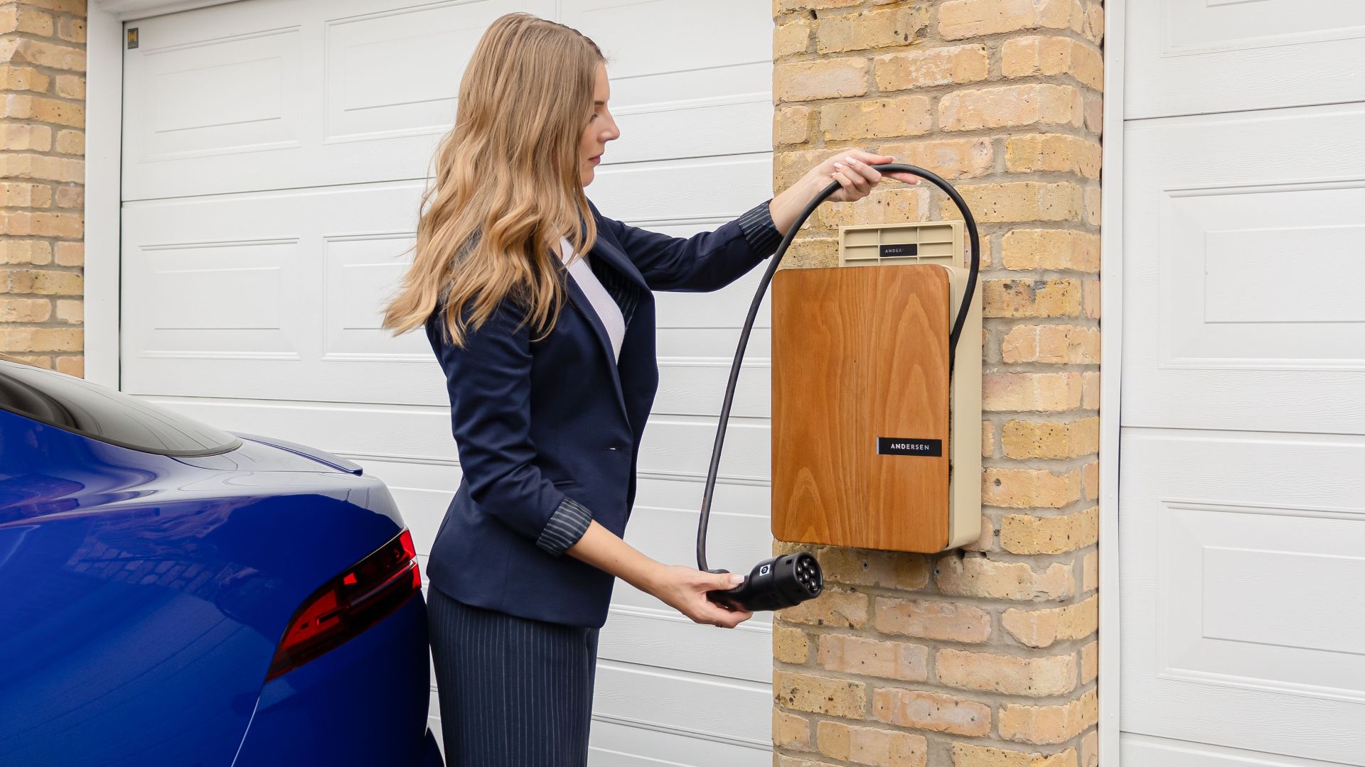 A woman using a home electric vehicle charger on a brick wall in a garage.