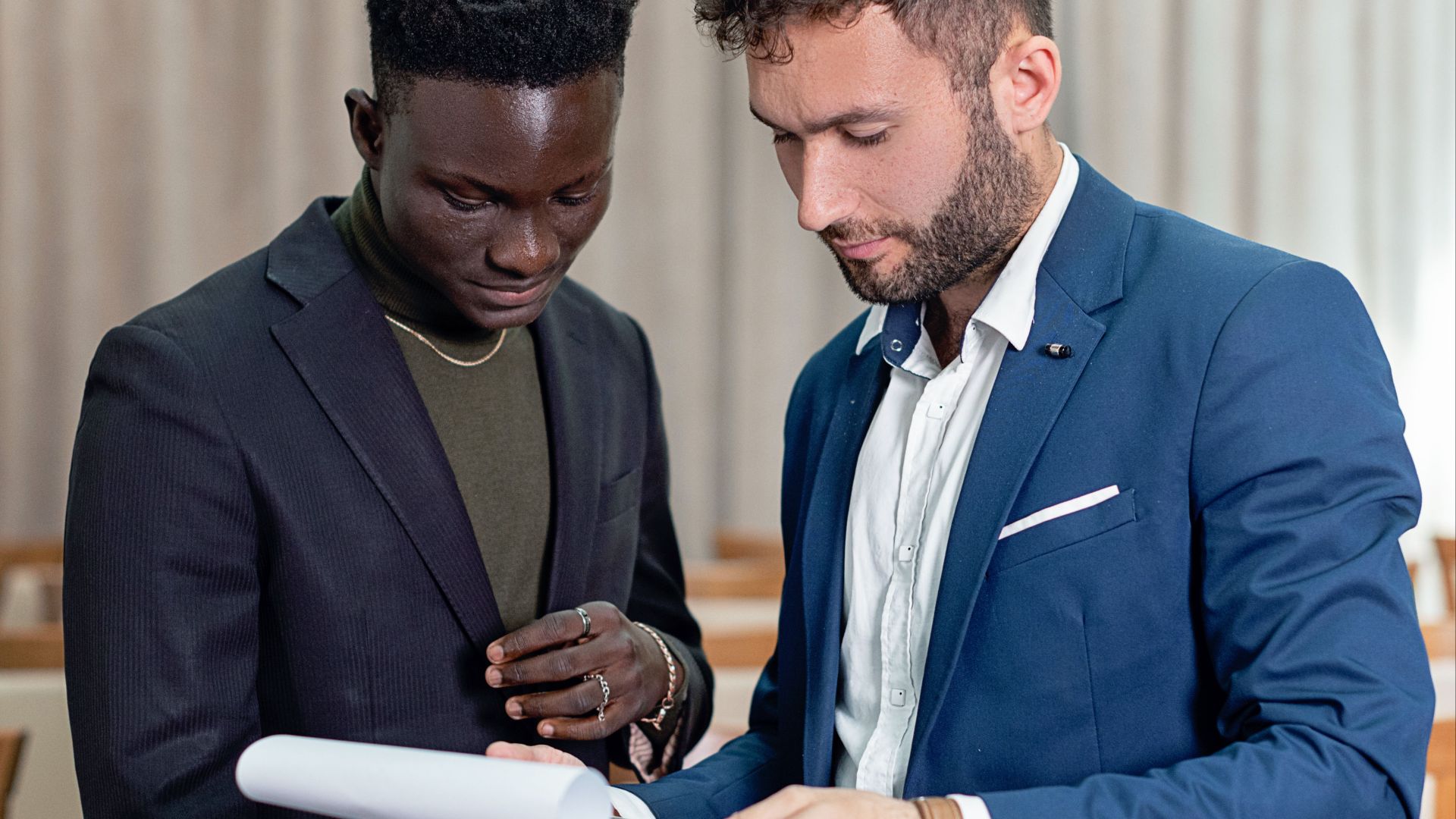 Two businessmen in suits review a contract indoors, focusing on the document.