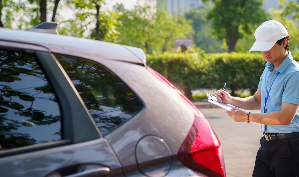 Car surveyor documenting vehicle damage after minor collision beside the road. Insurance officer evaluating auto insurance claims on-site and writing report on clipboard. Representing insurance services, safety, and claim processing.
