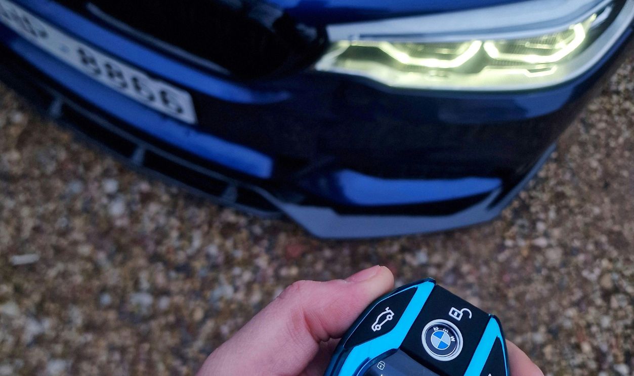 Luxury car key and parked vehicle in a gravel driveway, showcasing advanced features.