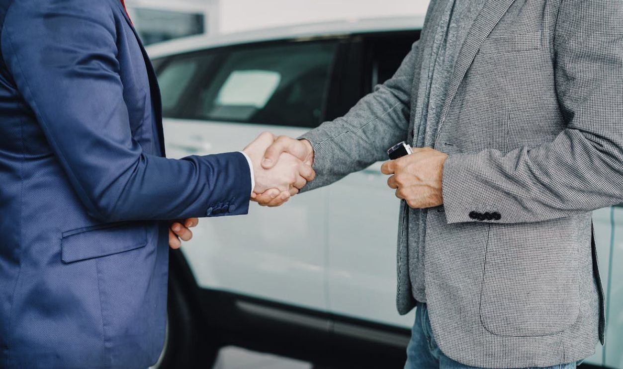 Two businessmen shaking hands in a car dealership, sealing a deal