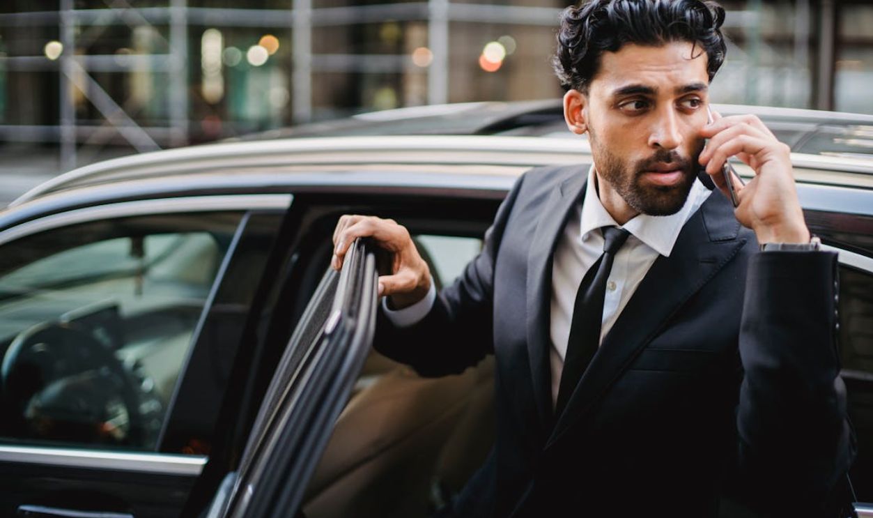 Confident businessman in a suit stepping out of a car while talking on the phone