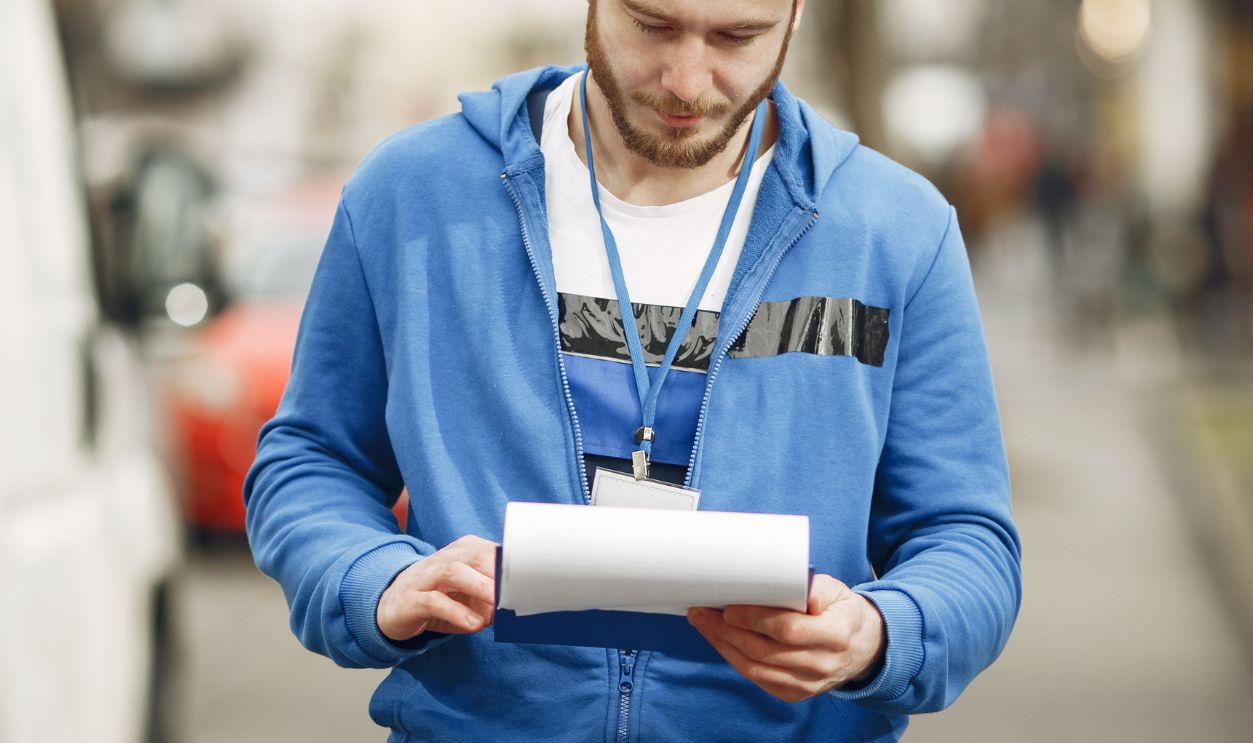 A delivery worker in blue uniform reading documents on a city street during the day