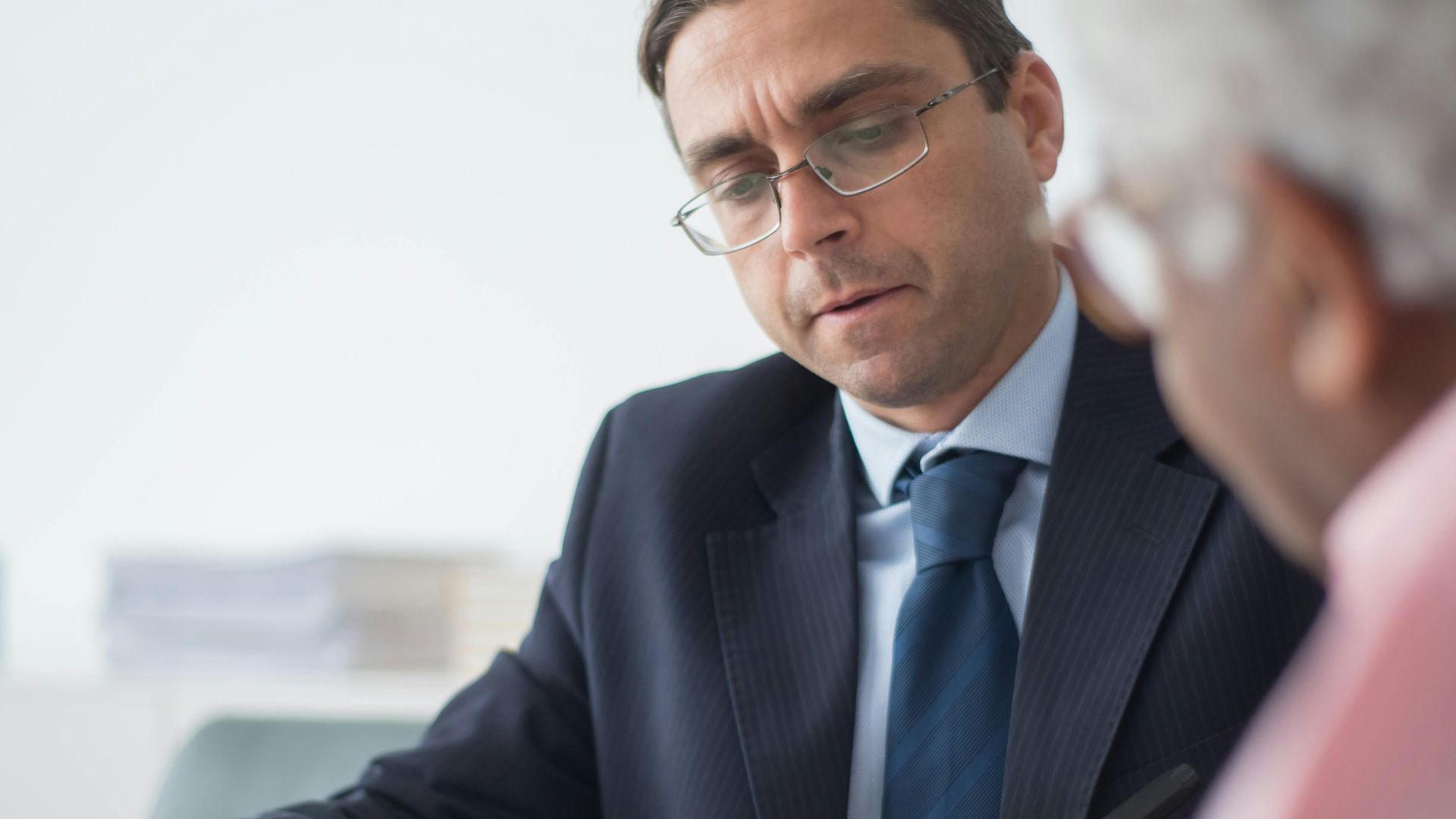 Senior man in discussion with consultant in office setting, reviewing documents.