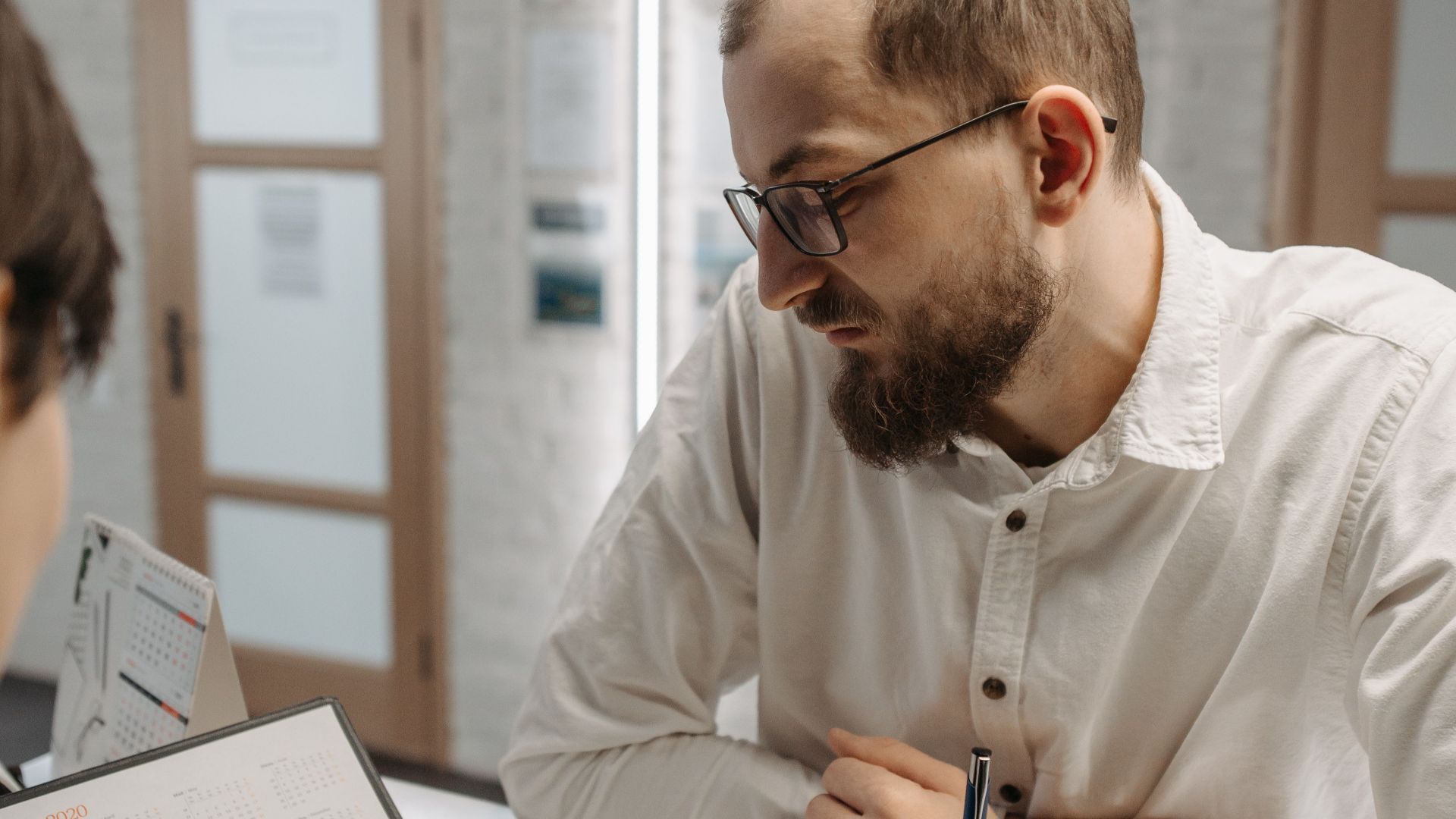 A thoughtful man leaning on a reception counter while discussing plans indoors.