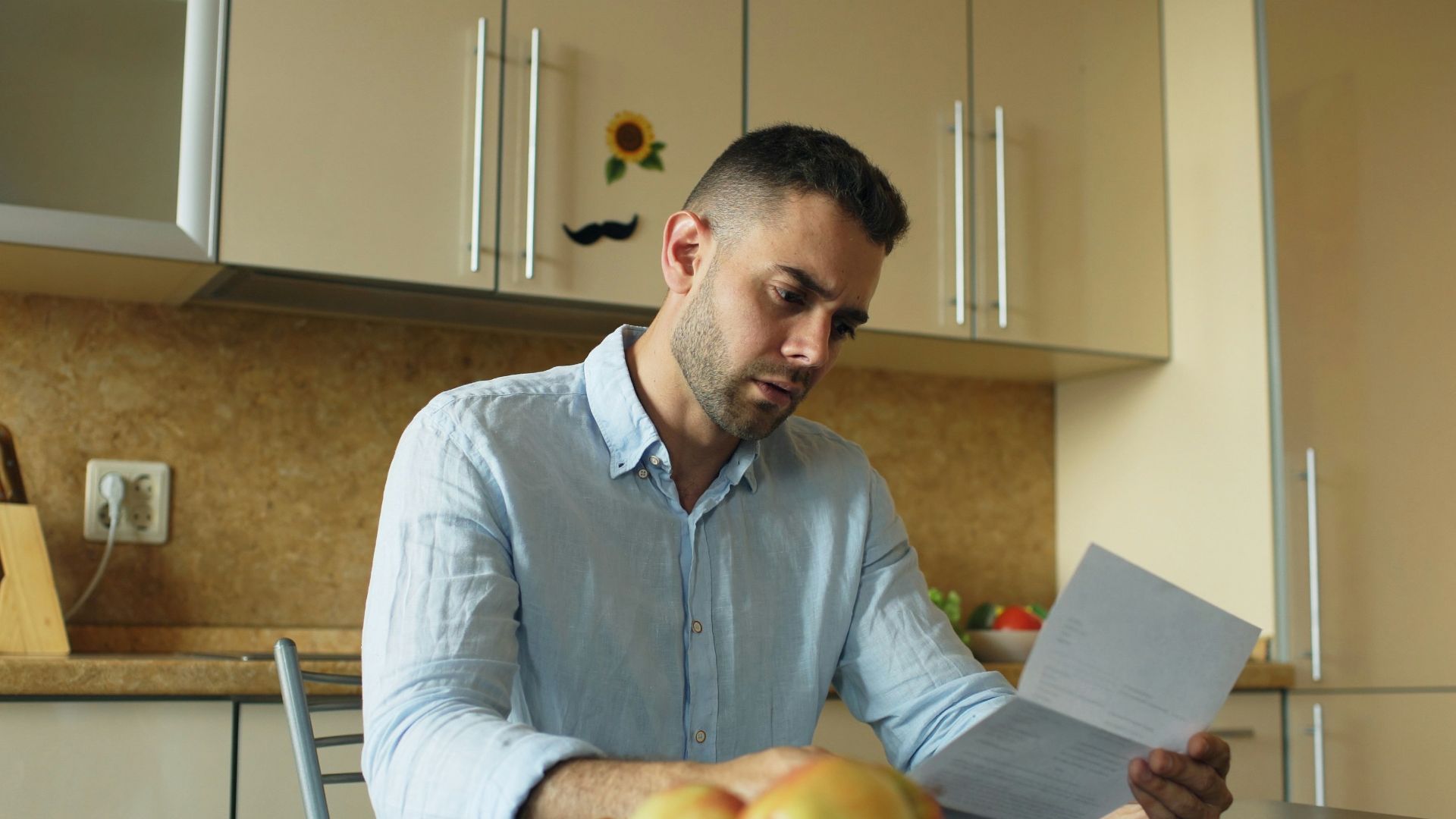 Man reading document at kitchen table with fruit and fruit