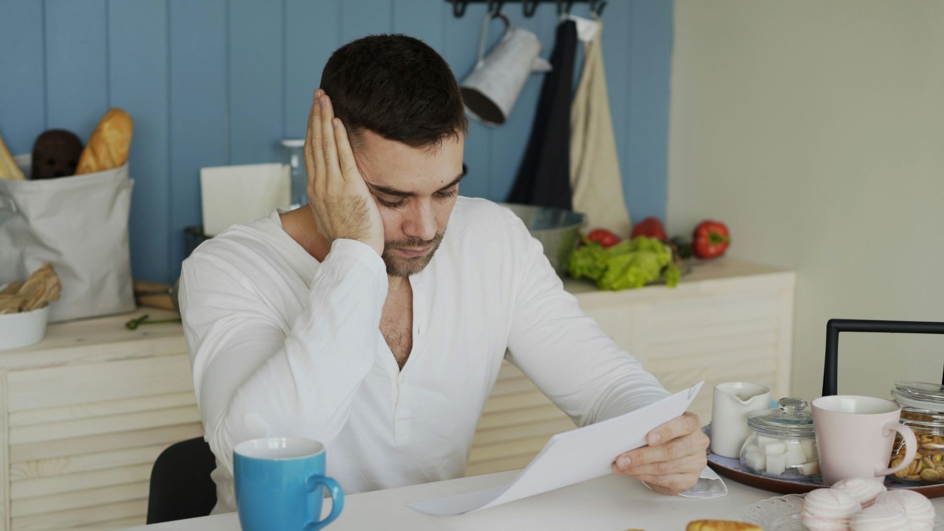 Man sitting at table reading papers with breakfast.