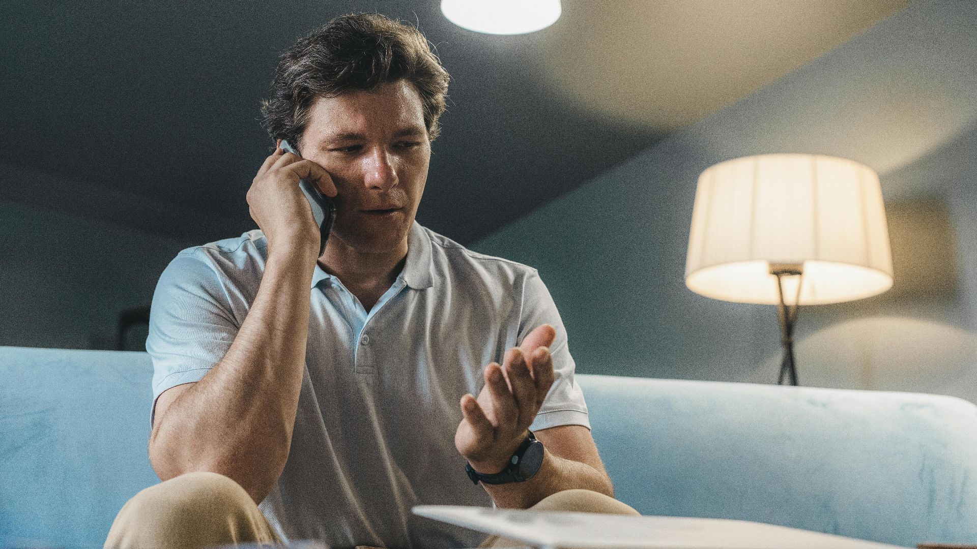 Man speaking on a smartphone while sitting on a sofa, working from home.