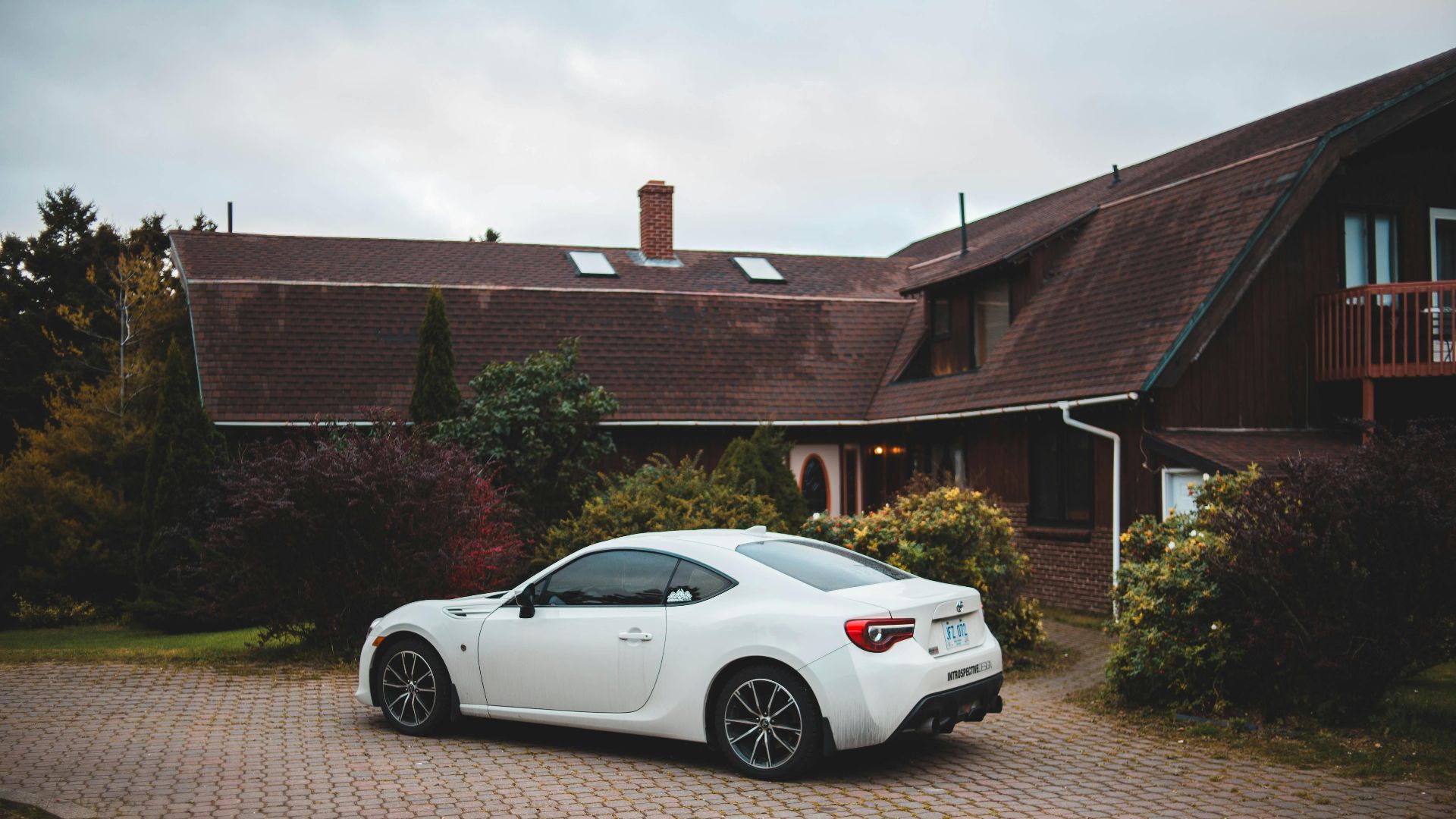A sleek white sports car parked in front of a charming rustic house with well-kept gardens.
